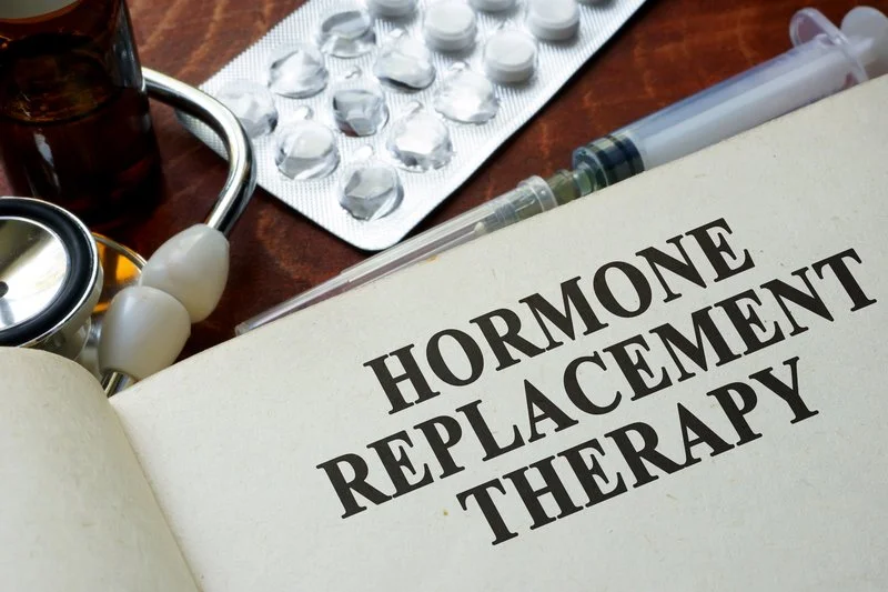 A book titled 'Hormone Replacement Therapy' on a desk with medication and medical supplies, including blister packs of pills, a stethoscope, and syringes.