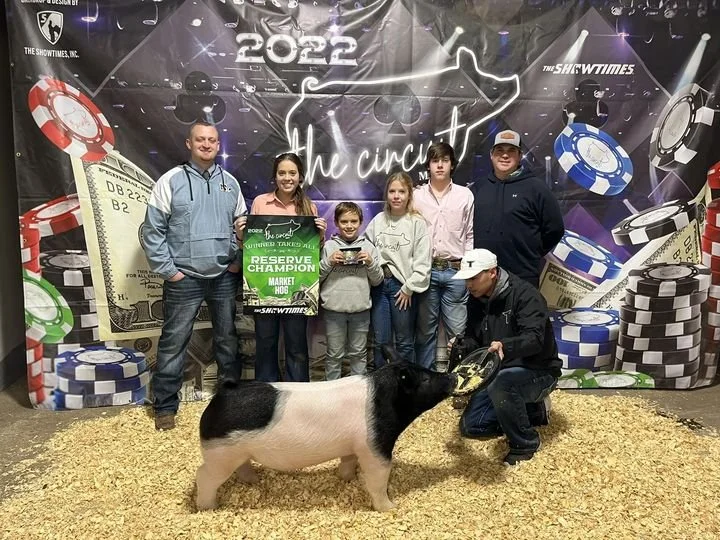 Group of people at a livestock competition with a pig, celebrating a reserve champion award, in front of a poker and money themed backdrop.