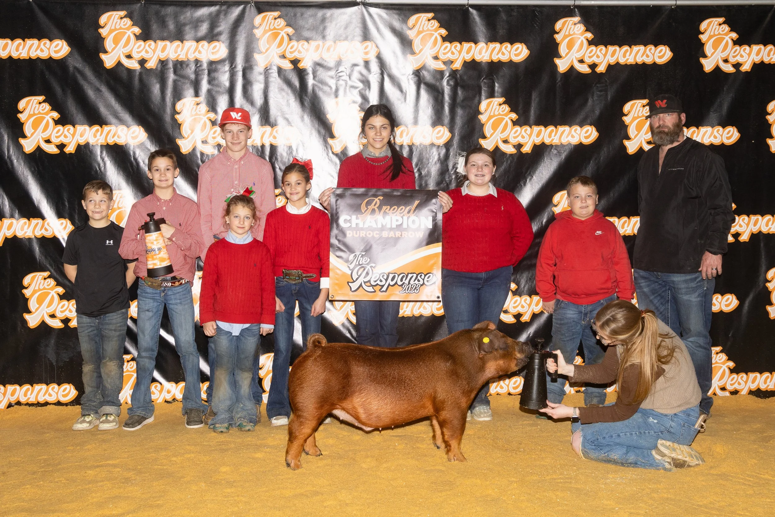 Kids and adults at a livestock show with a pig, holding a sign that says 'Breed Champion' for Duroc Barrow, photo taken at 'The Response' event.