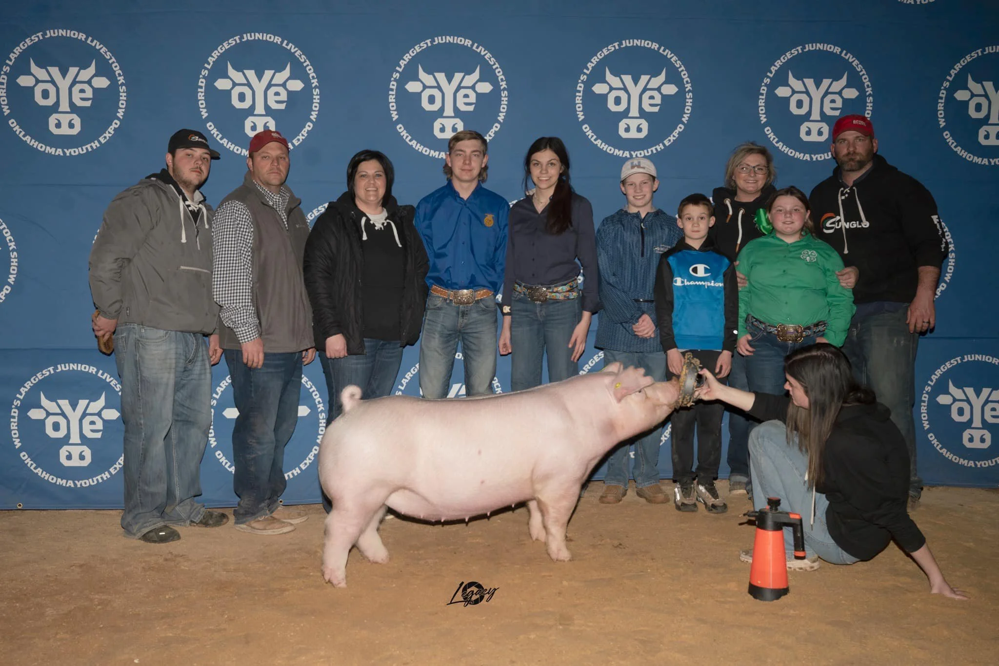 Group of people, including children and adults, at the Oklahoma Youth Expo, posing for a photo with a pig.