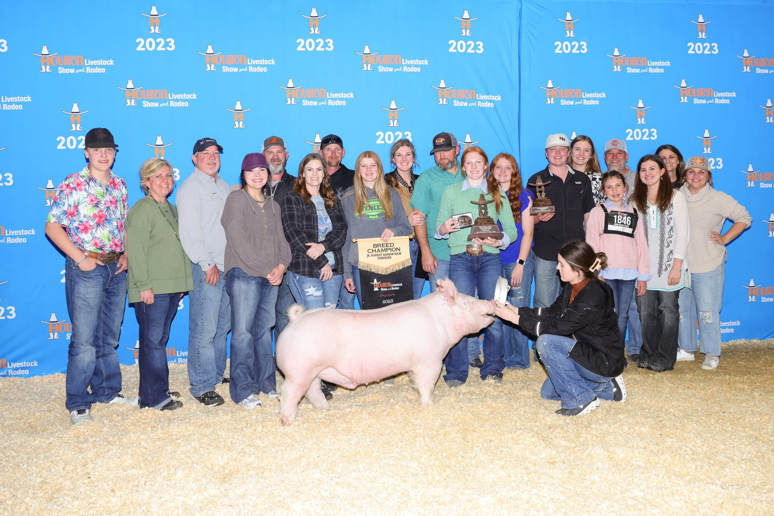 A group of people at the Houston Livestock Show and Rodeo 2023, posing with a pig in the foreground, some holding trophies and awards.