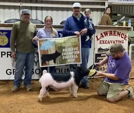 Group of five people at a livestock event, with a man kneeling in front holding a pig for a young woman and a young man. The pig won the reserve champion overall hog award.