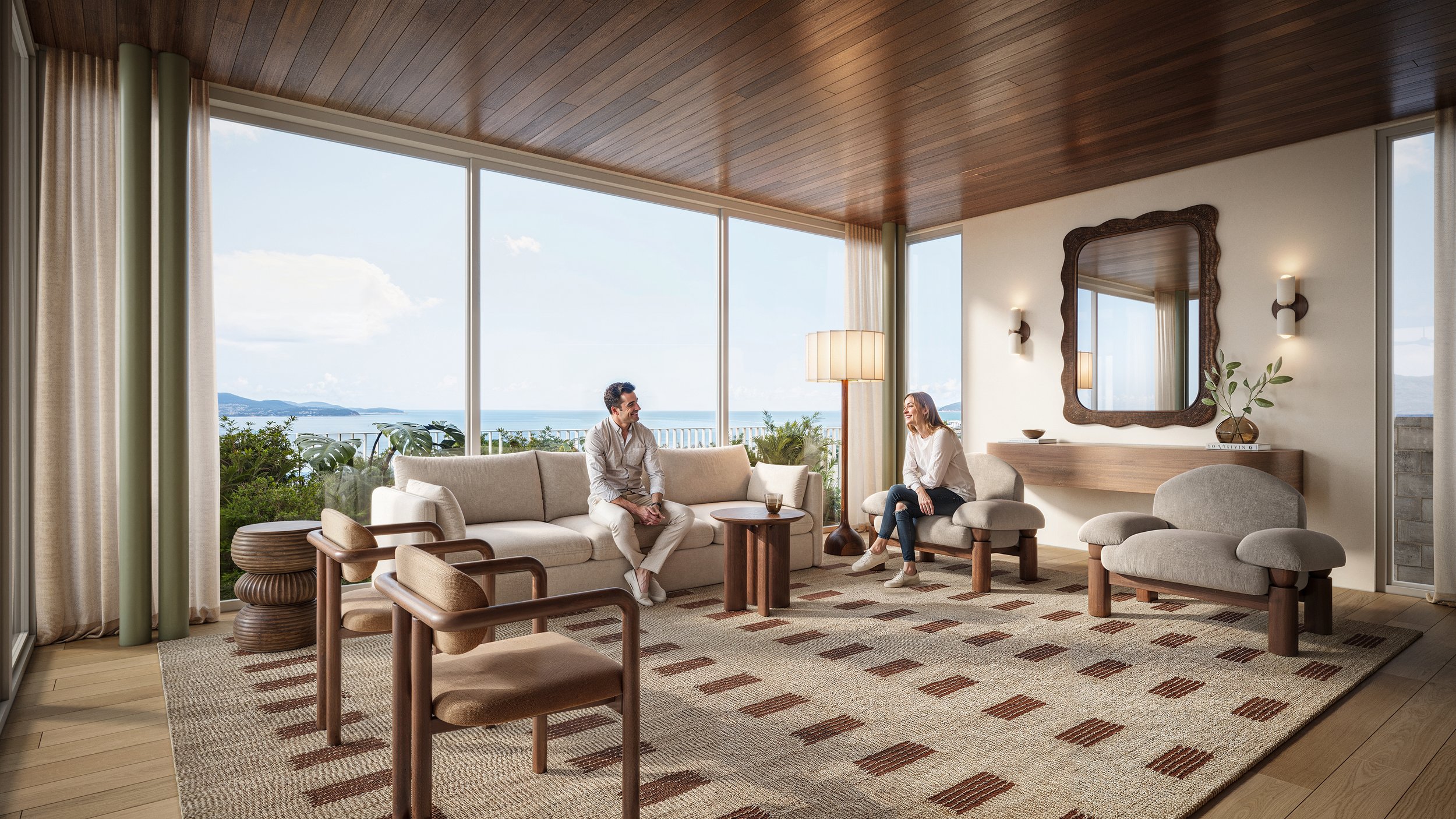 Living room with large windows showing ocean view, two people sitting on beige sofas, wooden ceiling, decorative mirror, plants, and patterned rug.
