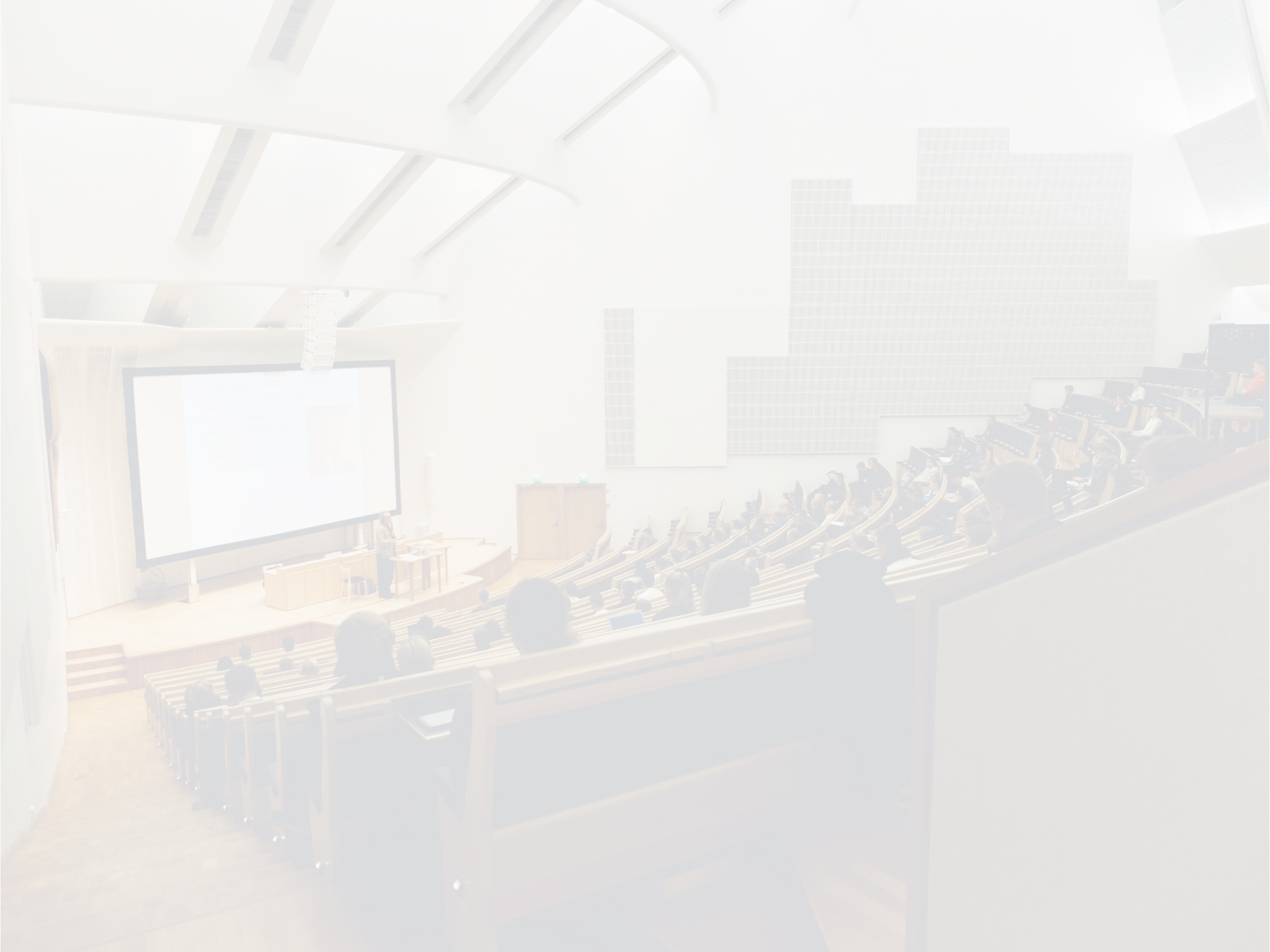 A modern lecture hall with tiered seating, a large screen, and few people seated, visible from the front.