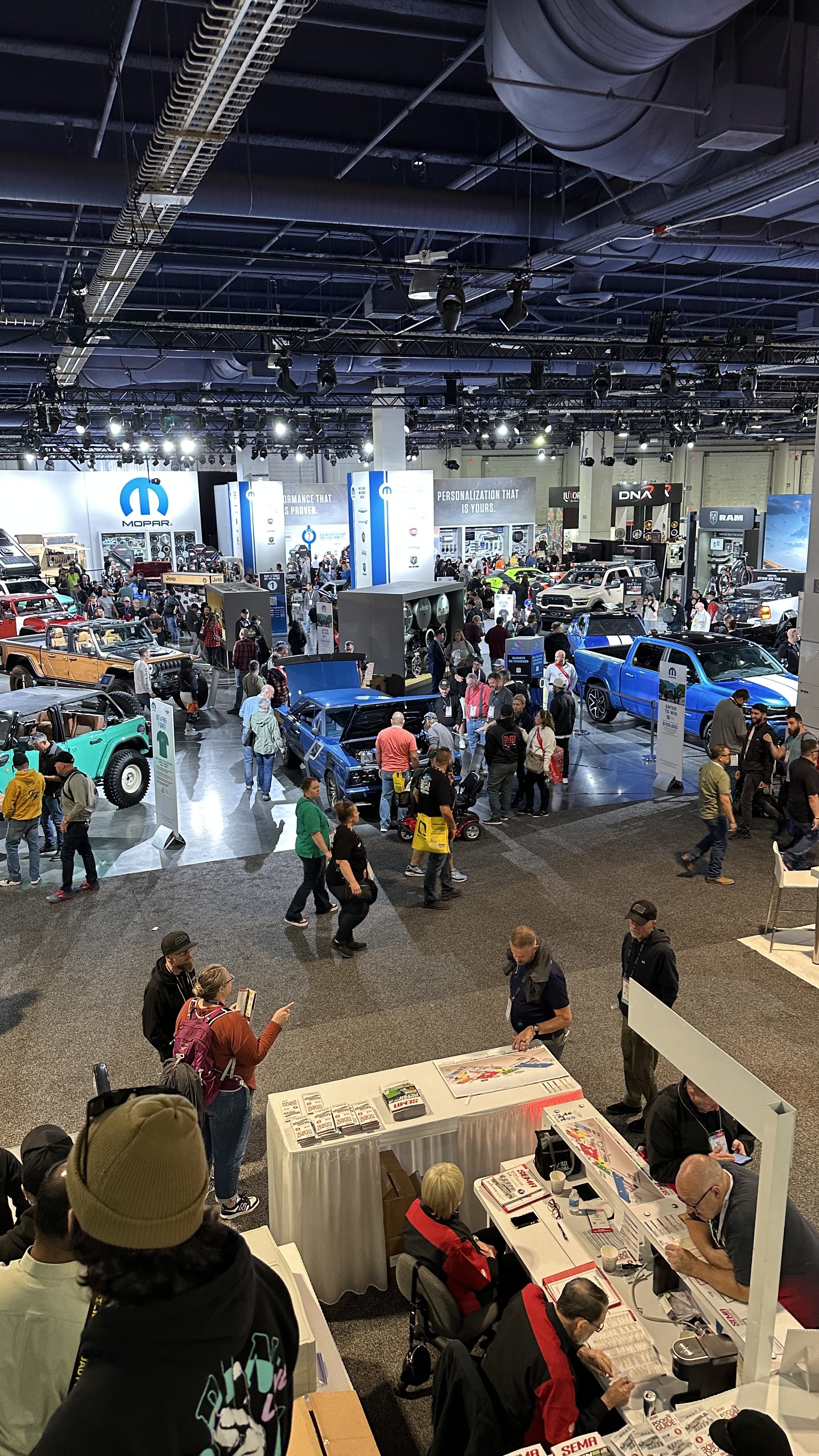 Indoor auto show with numerous vehicles and attendees exploring cars, booths, and displays, including brands like Jeep, Dodge, RAM, and Mopar.