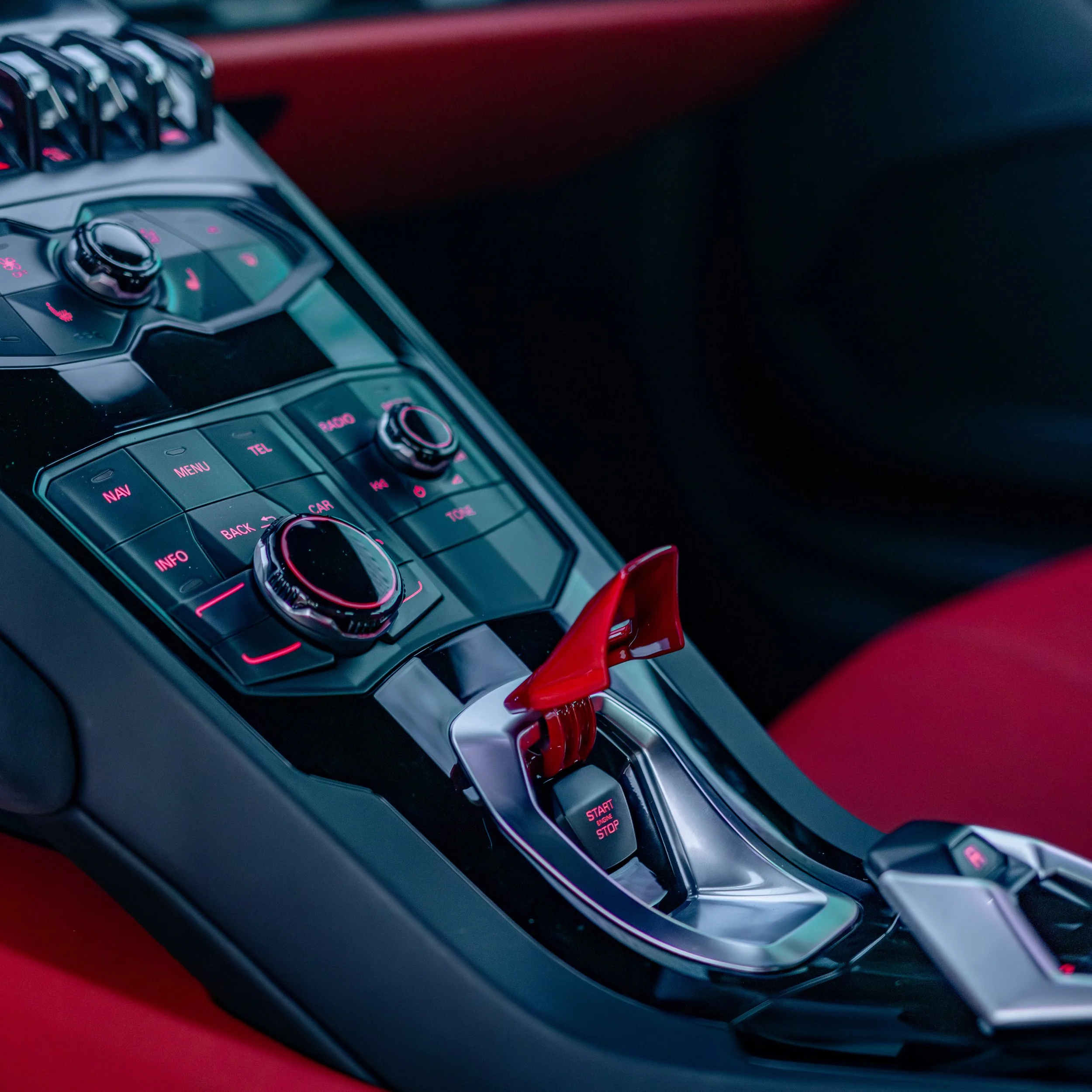 Close-up of a luxury car interior gear shifter and control panel featuring buttons and knobs with red and black accents.