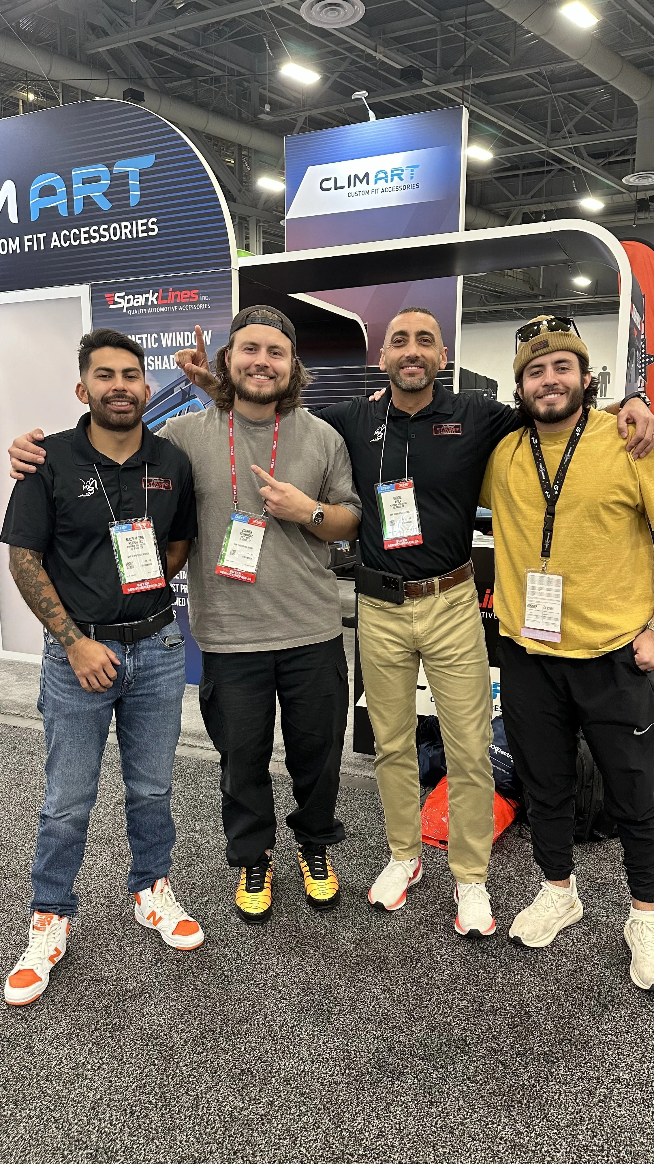 Four men standing together at a trade show, smiling and posing for the camera, with booths and signage in the background.