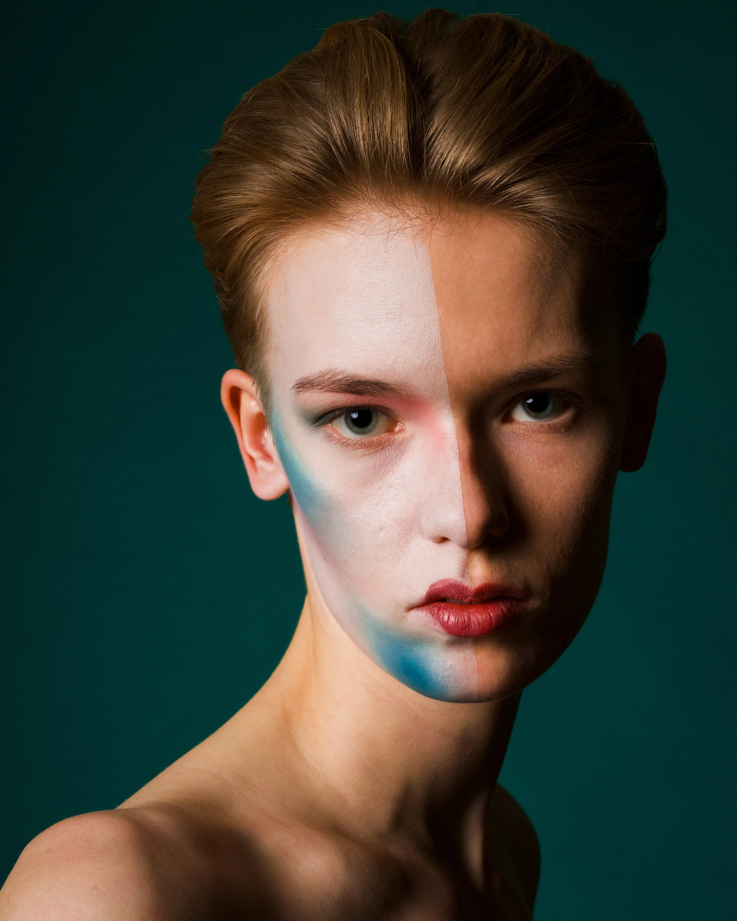 A young woman with half of her face painted with multicolored makeup, revealing a split face with natural makeup on one side and a painted artistic side on the other, against a dark background.