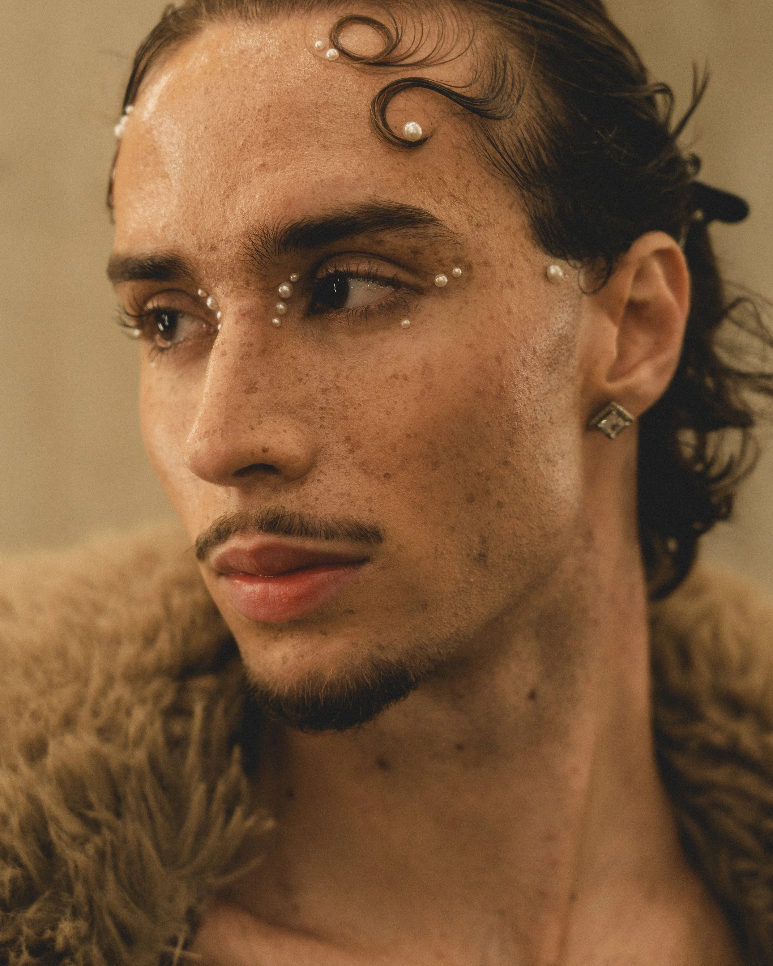 Close-up of a person with makeup decorated with pearls, wearing a fur coat and earrings, with afro-style hair.