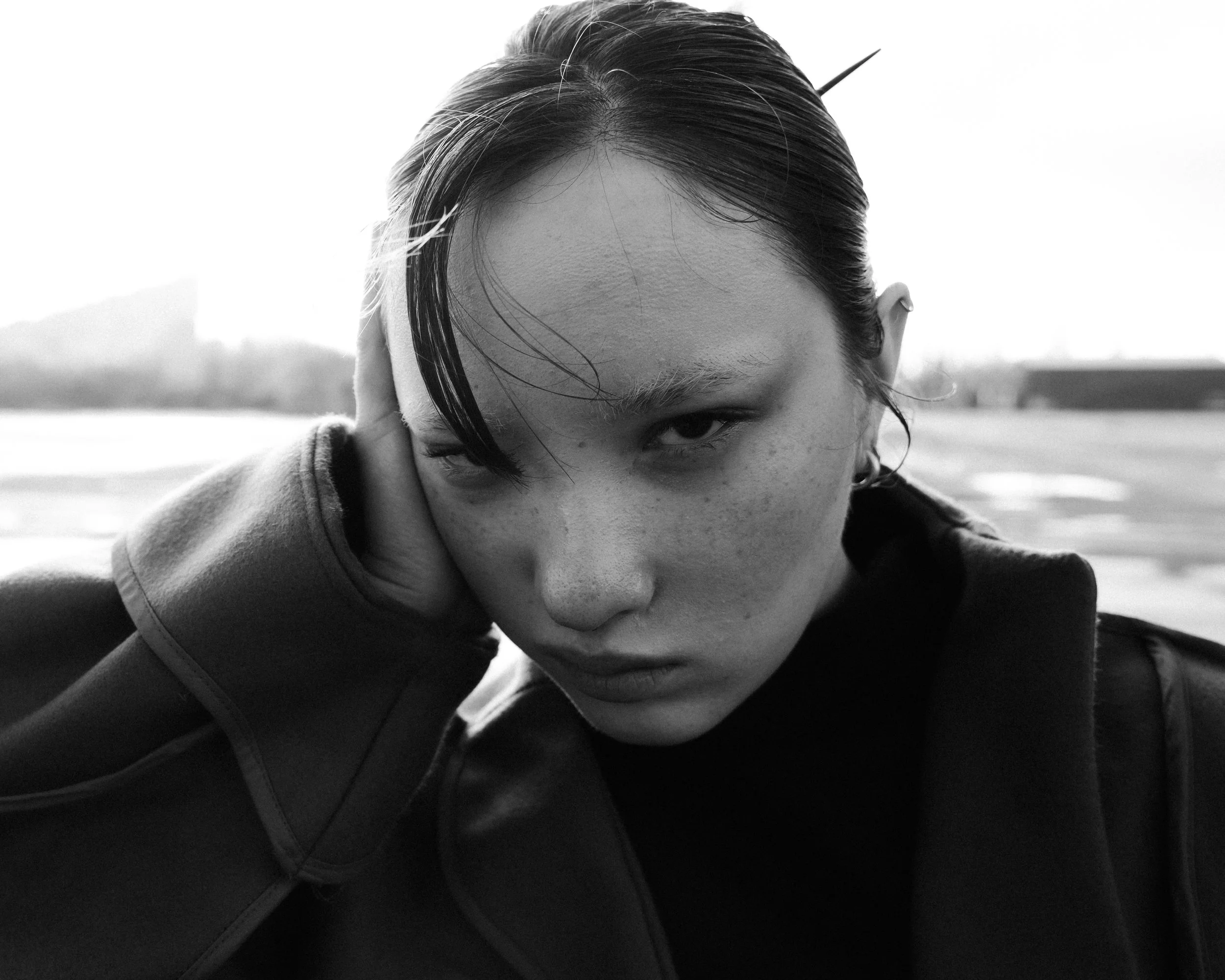 Black and white close-up portrait of a young woman with short, wet hair, piercing eyes, and a serious expression, outdoors in a natural setting.
