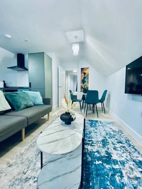 Modern living room with a gray sofa, teal pillows, marble coffee table, blue and white area rug, teal dining chairs, wall-mounted TV, and decorative wall art.