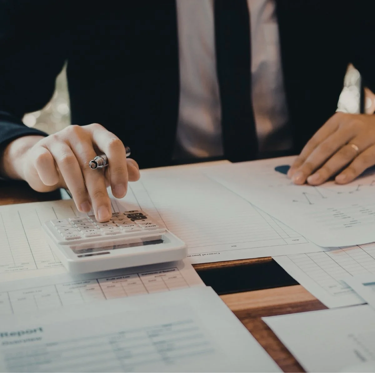 Person in business attire using a calculator on financial documents at a desk.