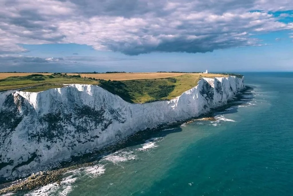 White chalk cliffs along the coastline with the ocean below and a partly cloudy sky above.