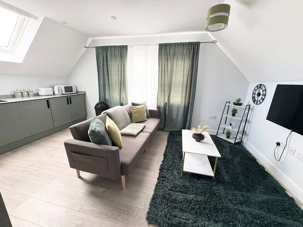 Modern living room with a gray sofa, curtains, flat-screen TV, and a white coffee table on a black rug.