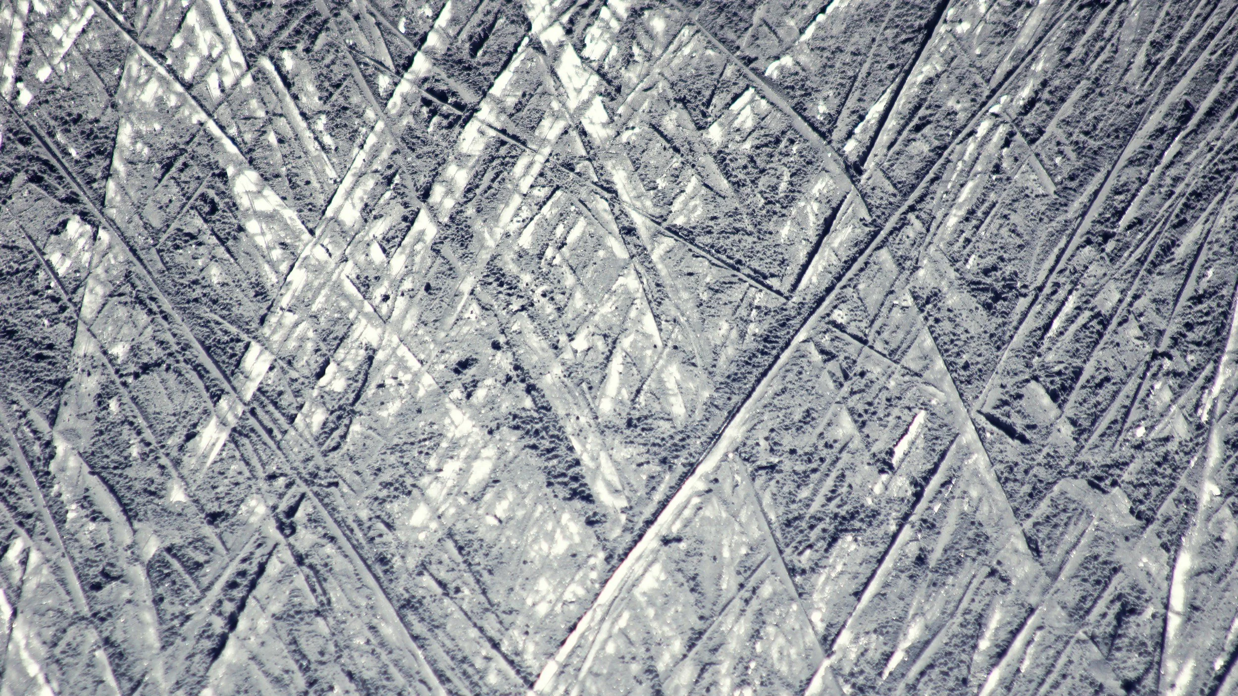 Close-up of imprints on ice surface, showing lines and patterns from skate marks or frozen water.