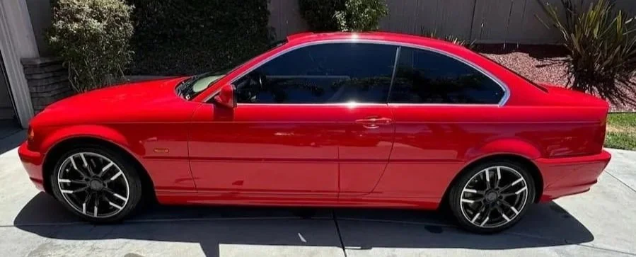 A cleaned red bmw parked on a driveway with dark tinted windows and sporty black rims. Sporting a clean look after a full auto detail.