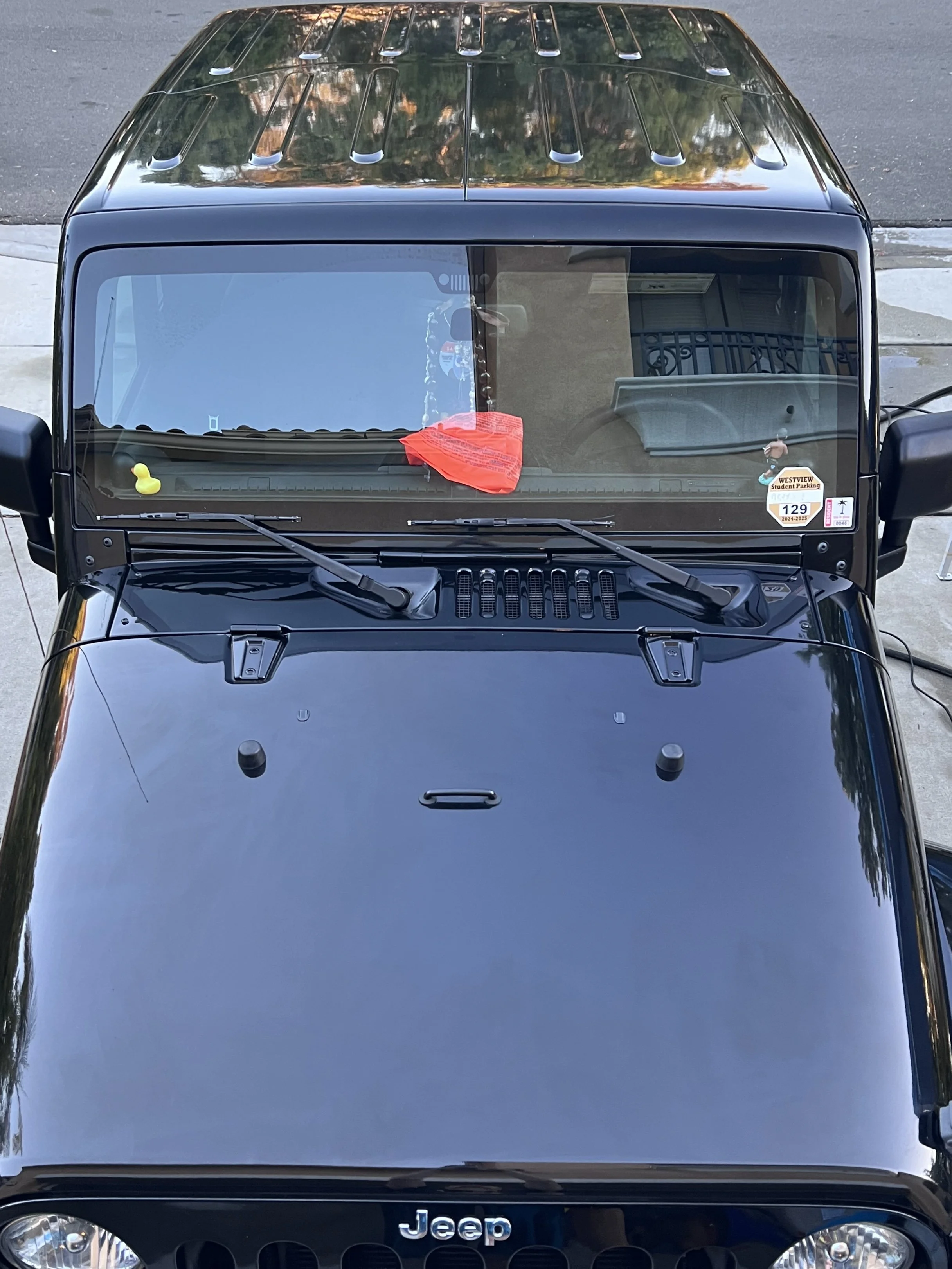 Top view of a black Jeep with a red cloth and yellow rubber duck on the dashboard, windshield wipers resting on the windshield.