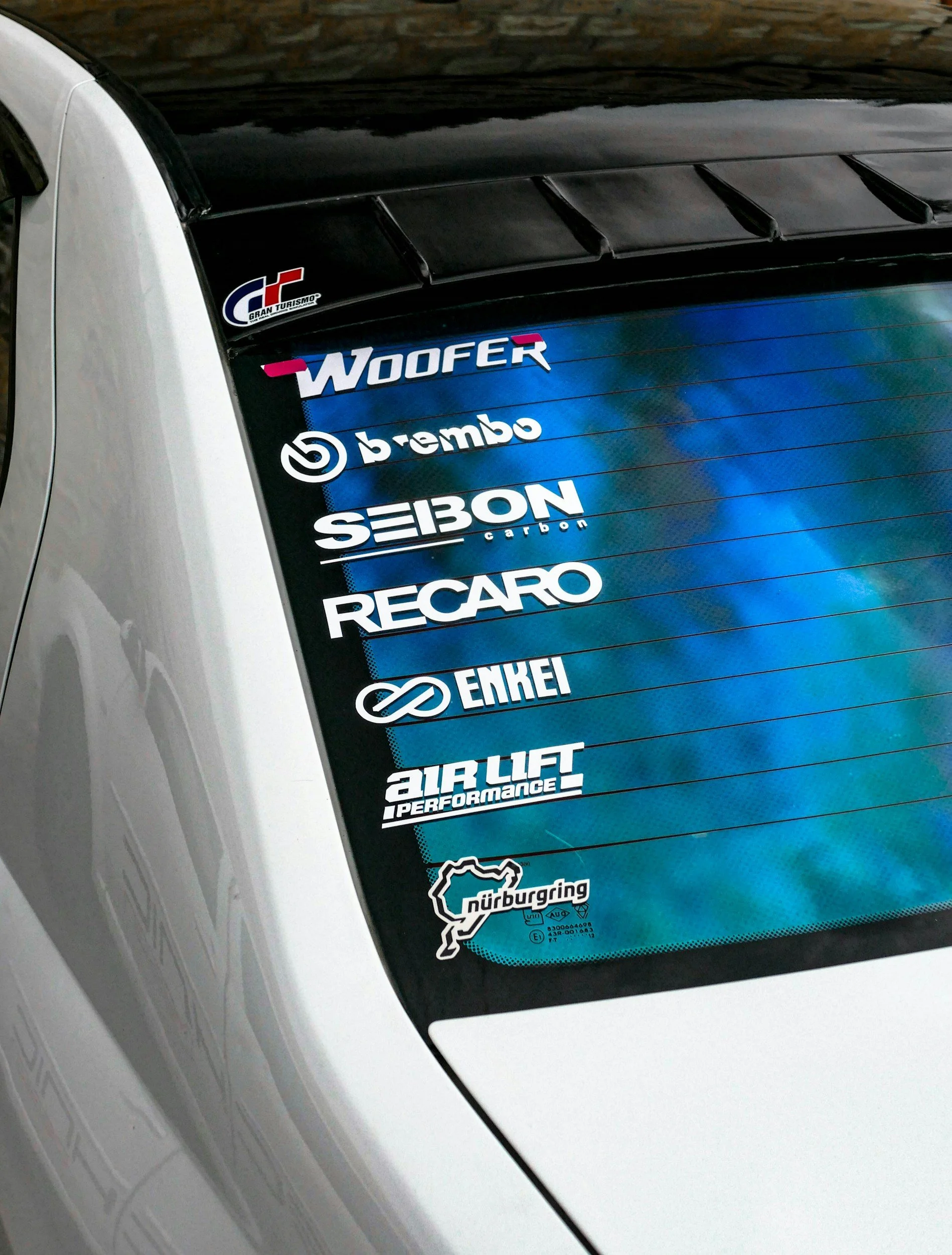 Car rear window with various sponsor decals, including Wofer, Brembo, Seibon, Recaro, Enkei, Air Lift Performance, and Nürburgring.