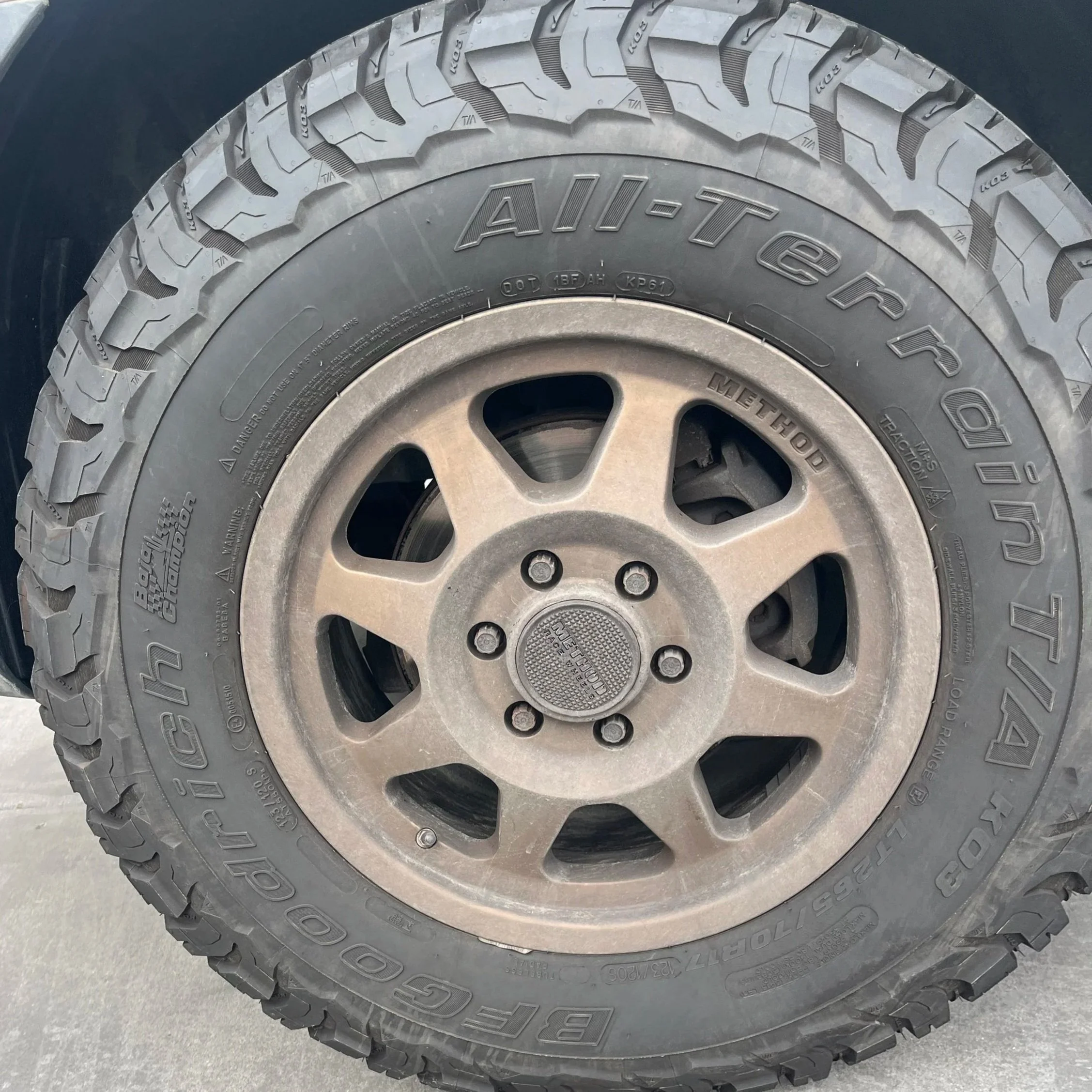 Close-up of a vehicle's tire with a rugged tread pattern, mounted on a silver-colored wheel with multiple ventilation holes. Before picture of a van tire during a detail in Del Mar, California.