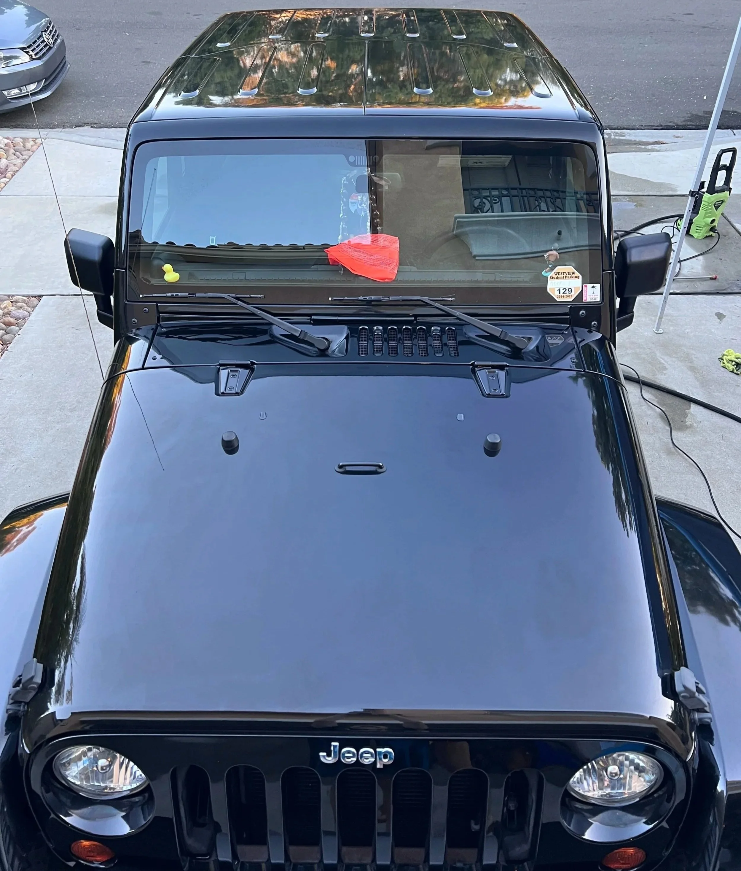 A black Jeep Wrangler parked on a driveway, seen from above, showing the front windshield, hood, and part of the roof. After picture of a jeep during a detail in Torrey Pines, San Diego.