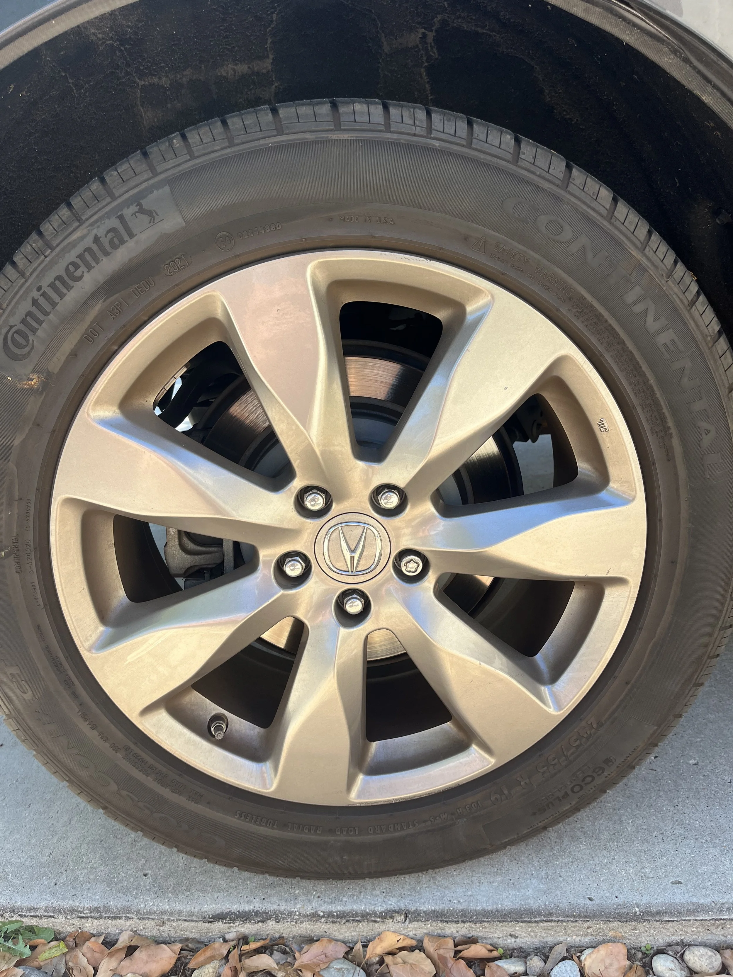 A car wheel with a silver alloy rim and a black tire, with the Honda logo in the center. A before photo of tire during a detail in Rancho Penasquitos.