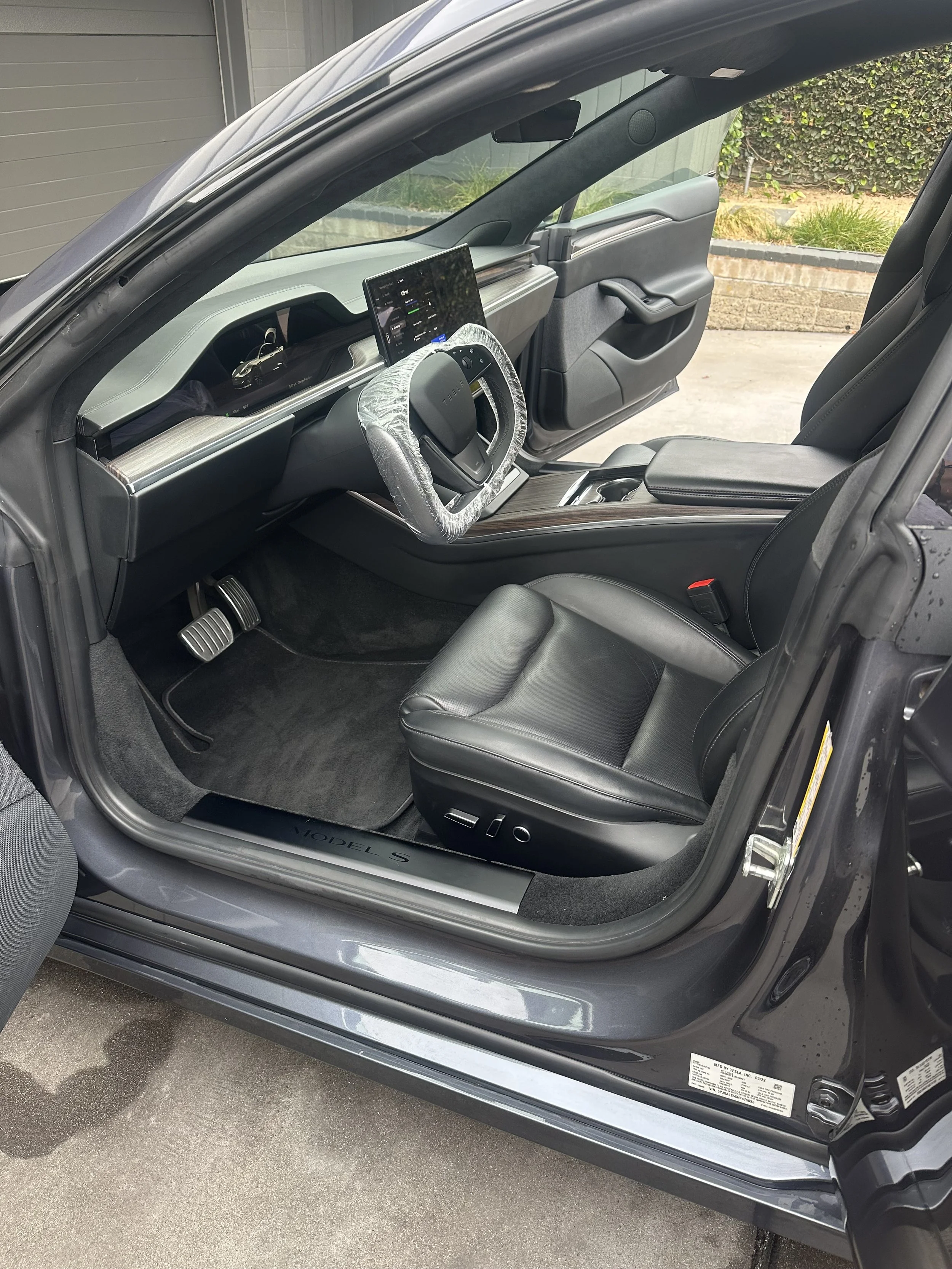 The interior of a modern electric vehicle showing a digital dashboard, modern steering wheel, driver's seat, and center console with wood trim.