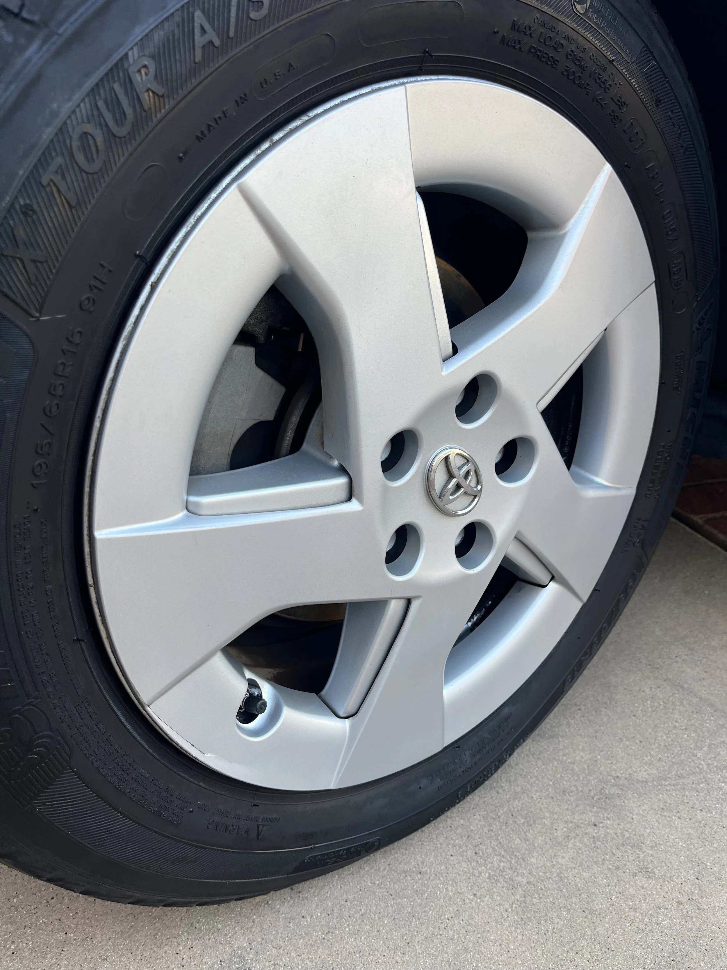 A close-up of a silver Toyota car wheel with a tire mounted on it, showing the Toyota logo at the center cap. After picture of a sedan tire during a detail in Poway, California.