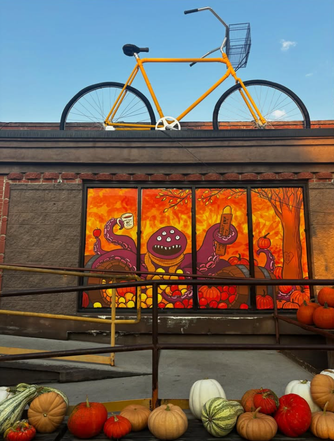 Colorful mural featuring a friendly monster with multiple eyes, holding a drink and a popsicle, surrounded by pumpkins and autumn leaves, with a bright orange background.