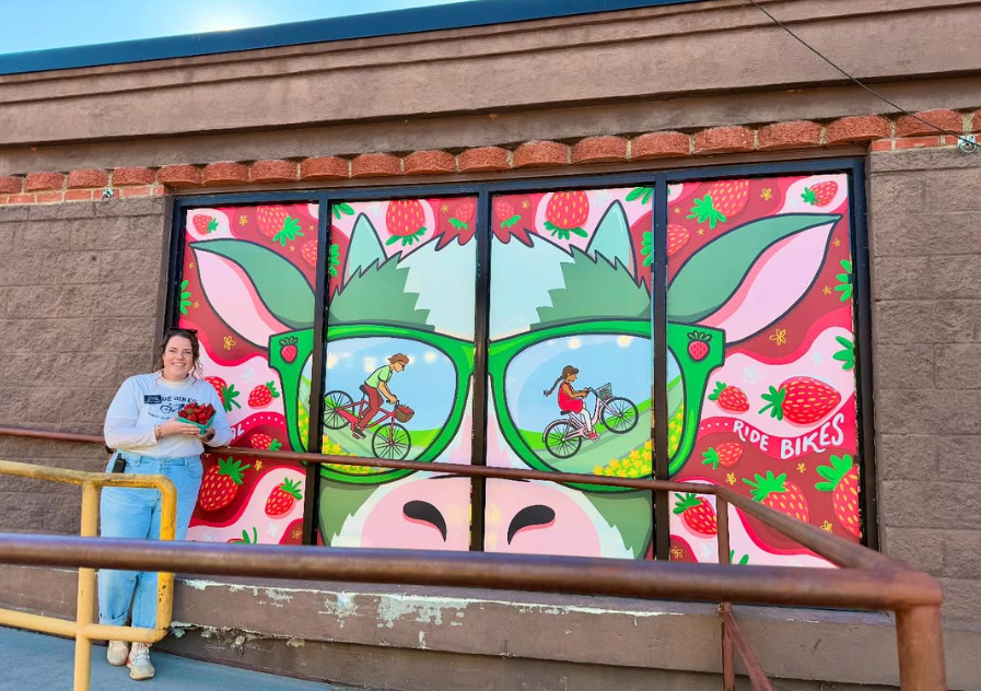 Colorful mural of a mountain goat with large pink and green strawberries on its face, and two people riding bikes inside the goat's nose, with the phrase 'Ride Bikes' on the right side.