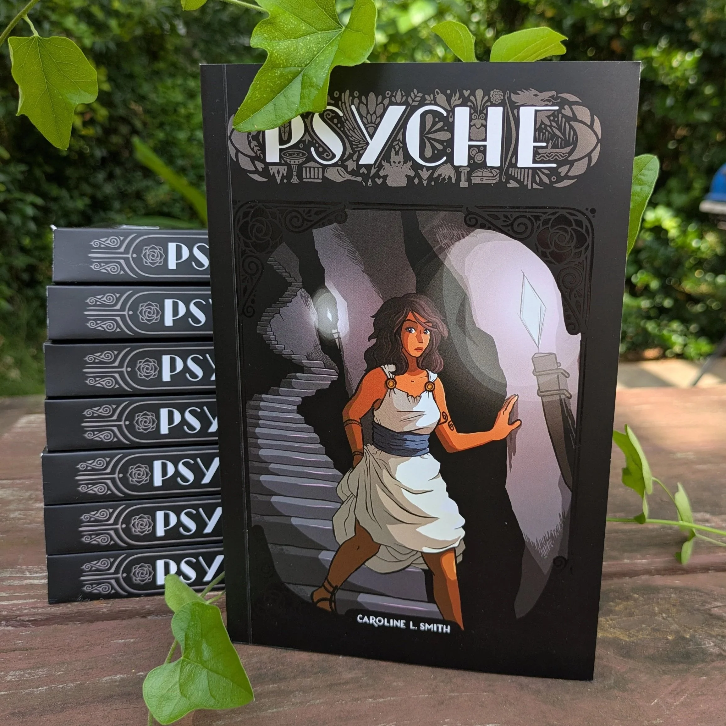 A book cover titled 'PSYCHE' by Caroline L. Smith featuring an illustrated woman in ancient Greek attire with dark hair, standing in a dark cave with a staircase and glowing lights.