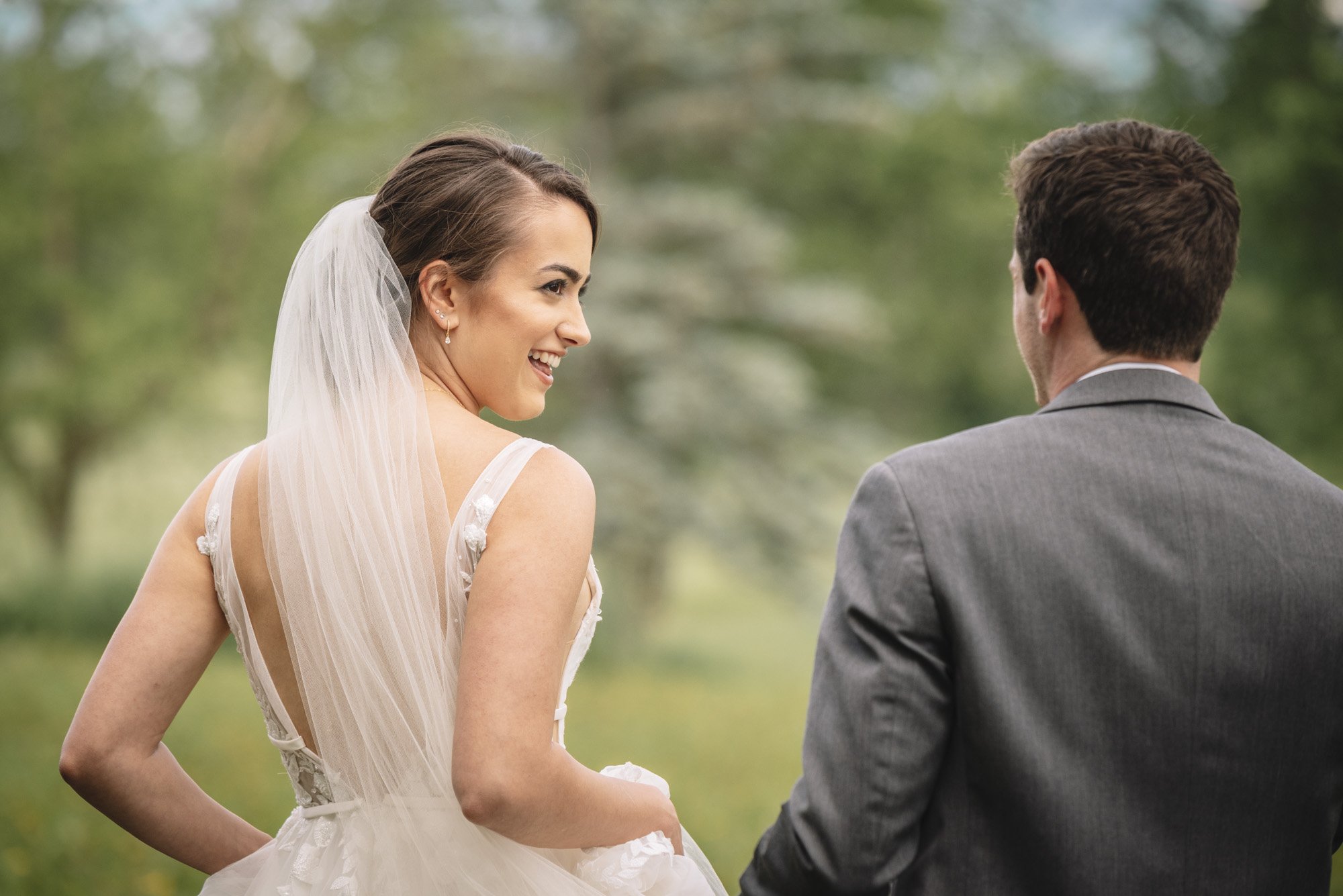 A bride and groom are outdoors, facing each other with the bride smiling and turning her head to the left.