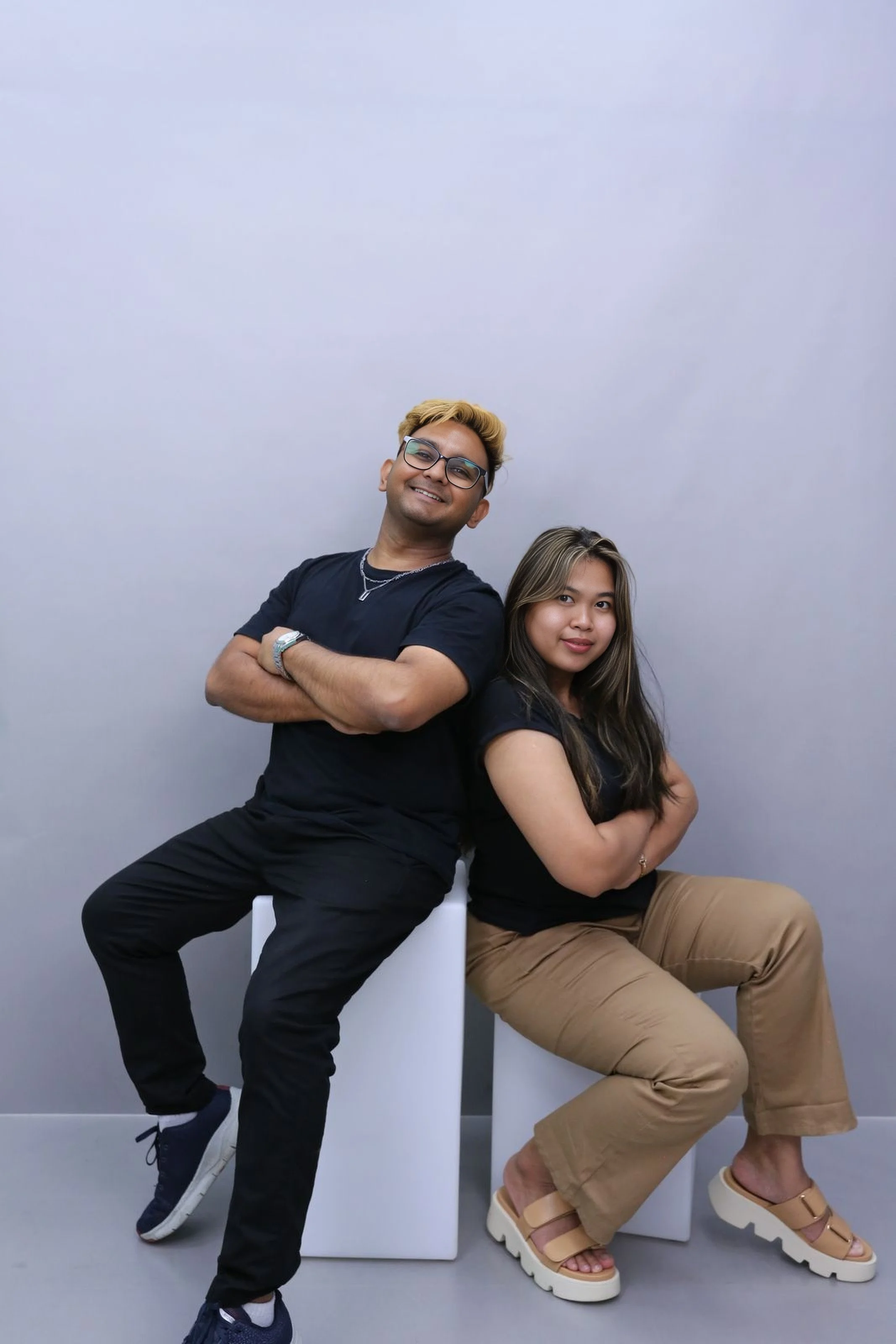 Two people sitting at a table, one working on a laptop and the other taking notes in a notebook, with a glass of water and a vase with white flowers on the table.