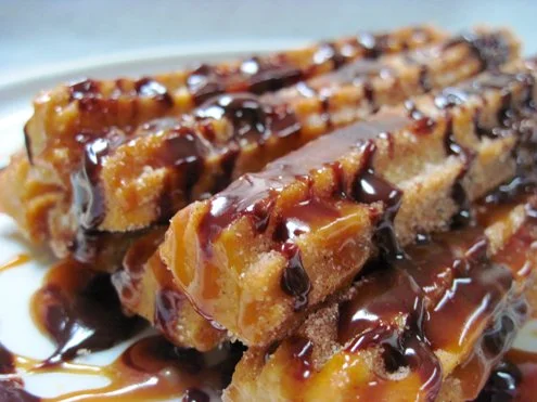Stacked caramel and chocolate dessert bars drizzled with chocolate syrup.