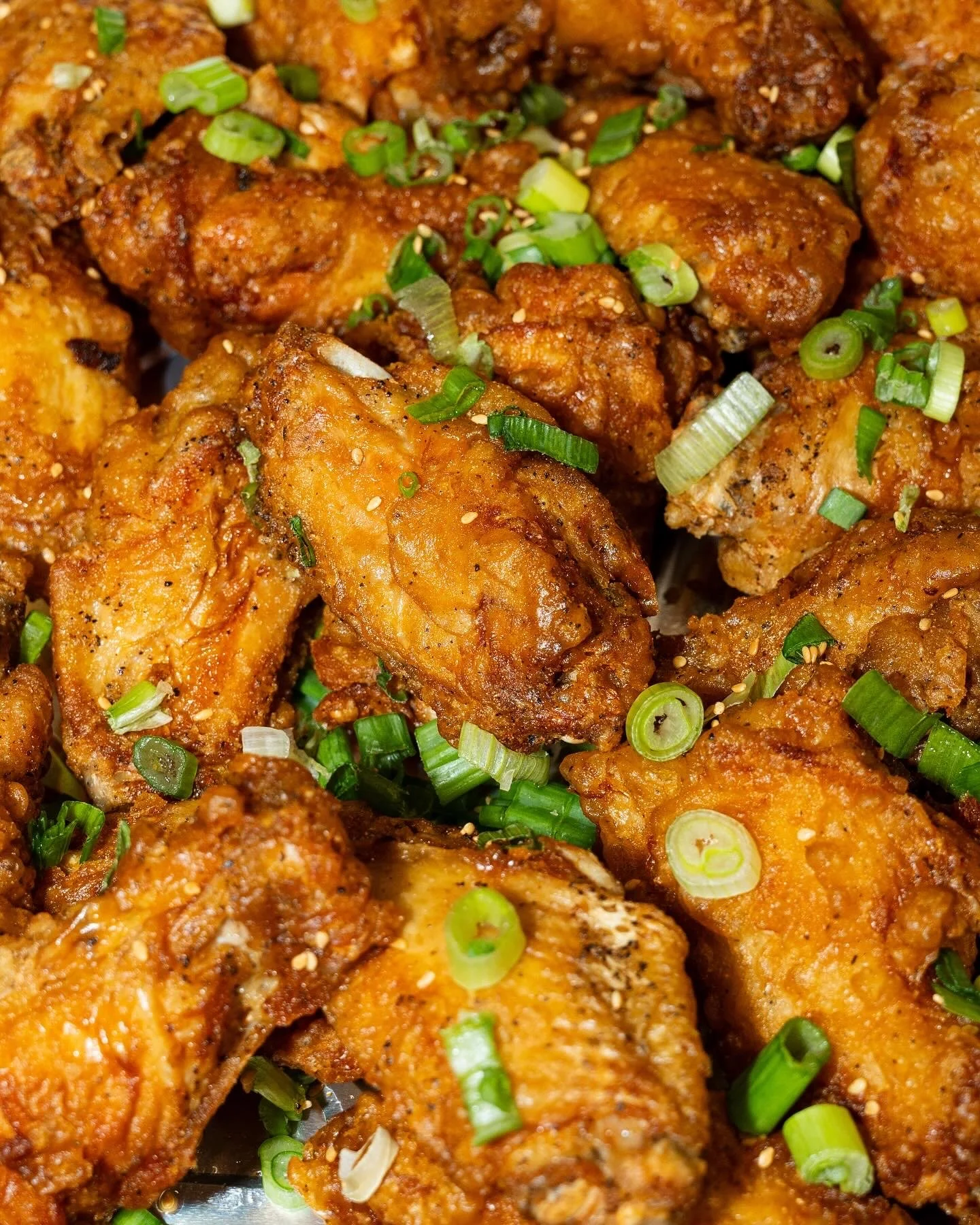 Close-up of crispy fried chicken drumsticks garnished with chopped green onions.