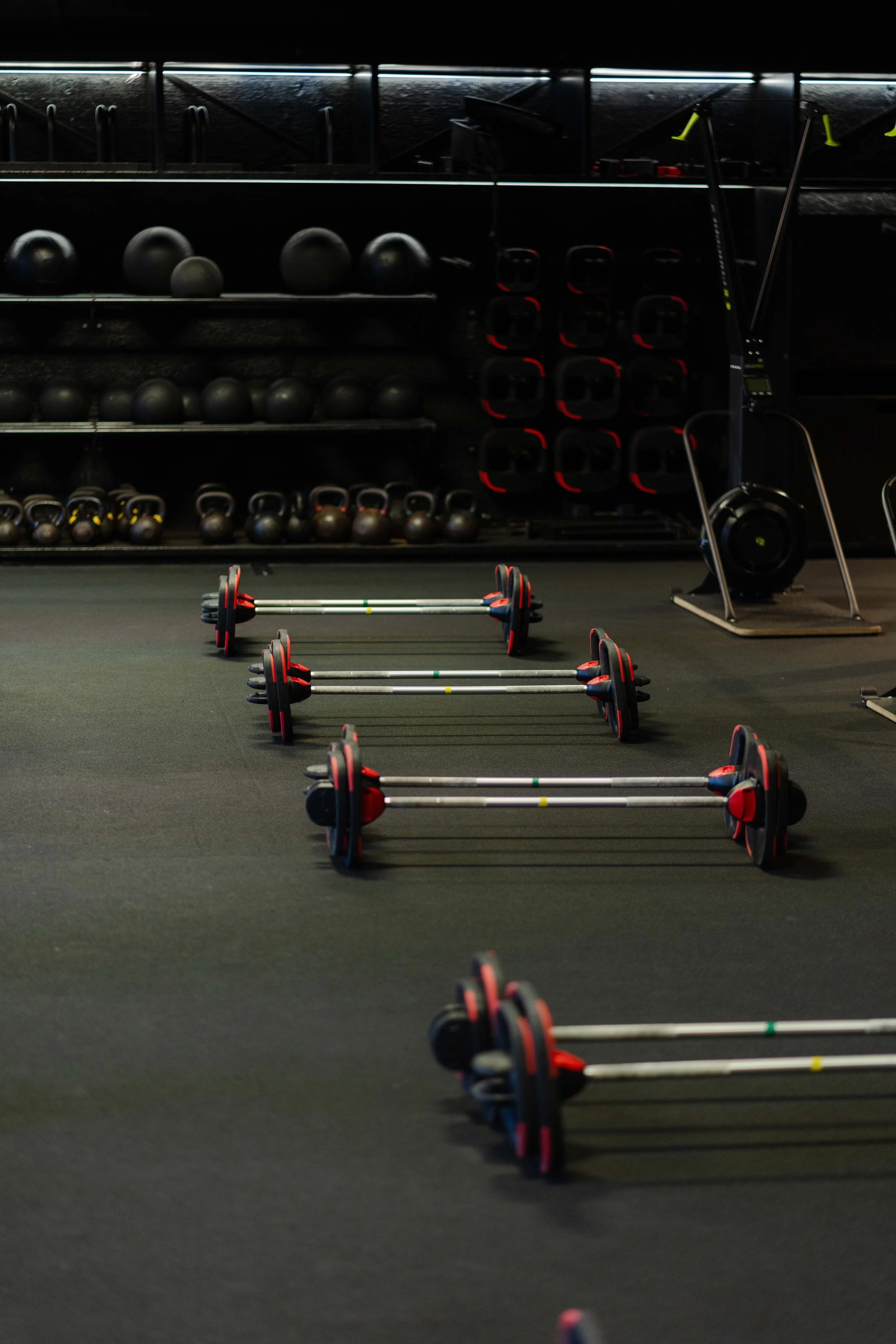 Multiple rowing machines lined up on the floor of Les Mills gym or fitness studio with black exercise balls and weight plates stored on shelves in the background.