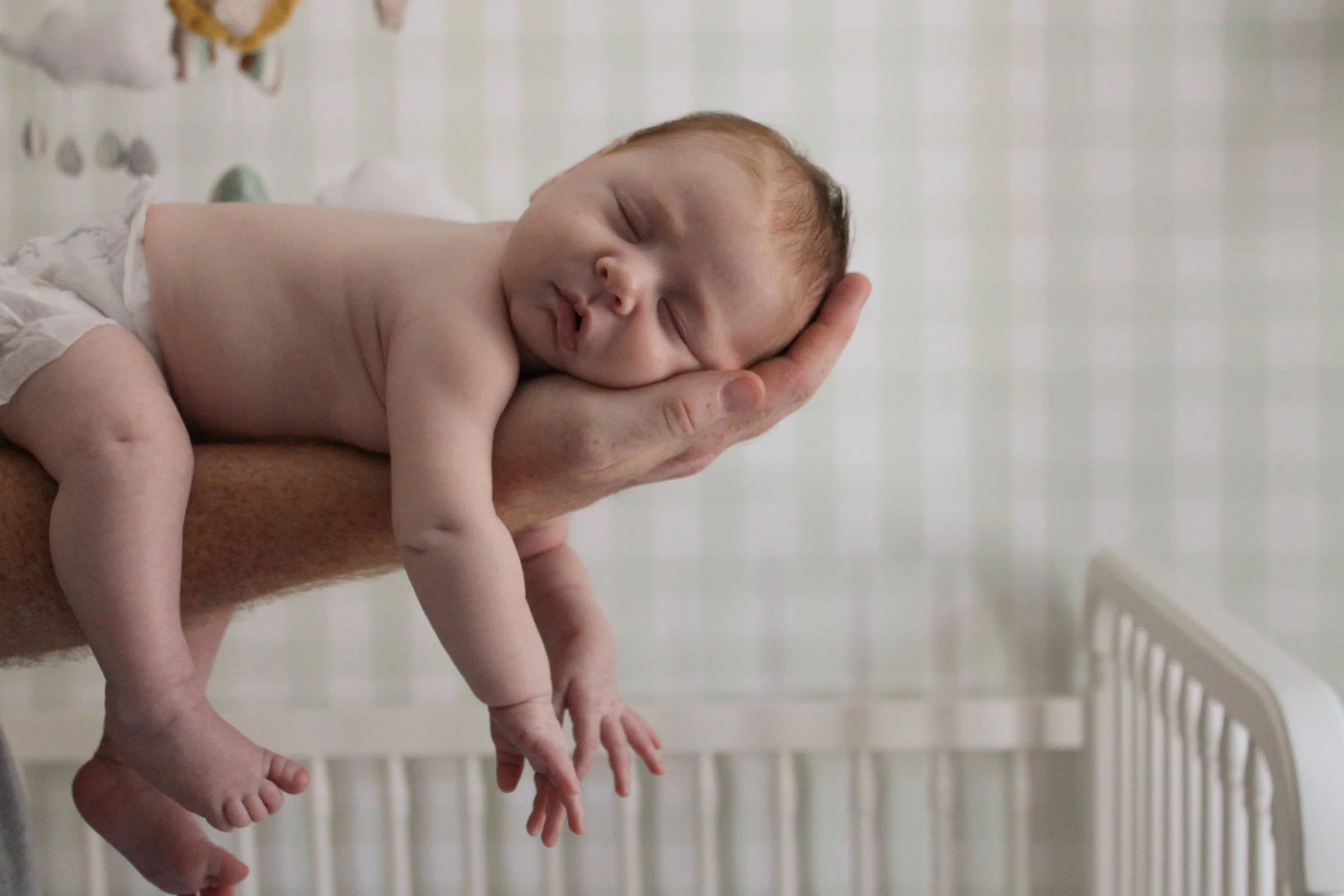 A newborn baby sleeping on a person's hand in a crib.