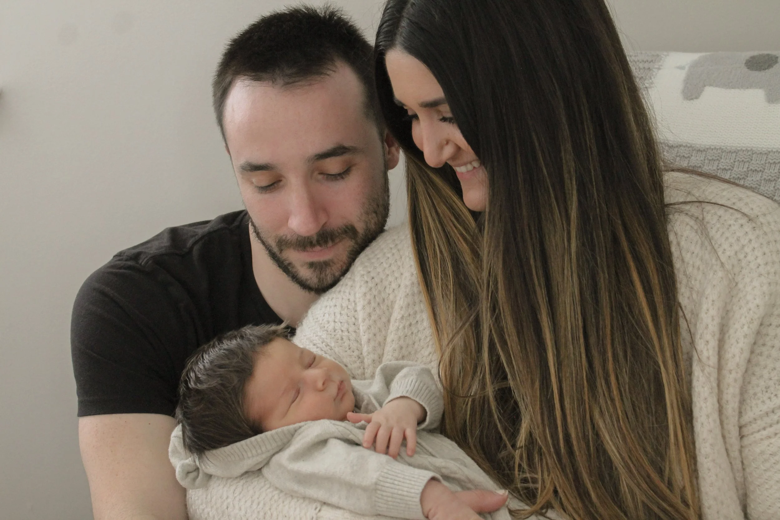 A couple holding a newborn baby indoors, both looking lovingly at the baby.
