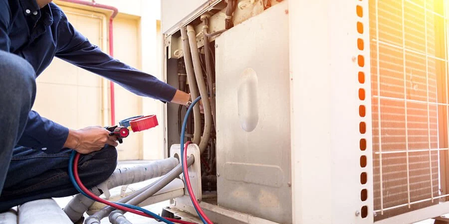 Person repairing an air conditioning unit using a digital multimeter.