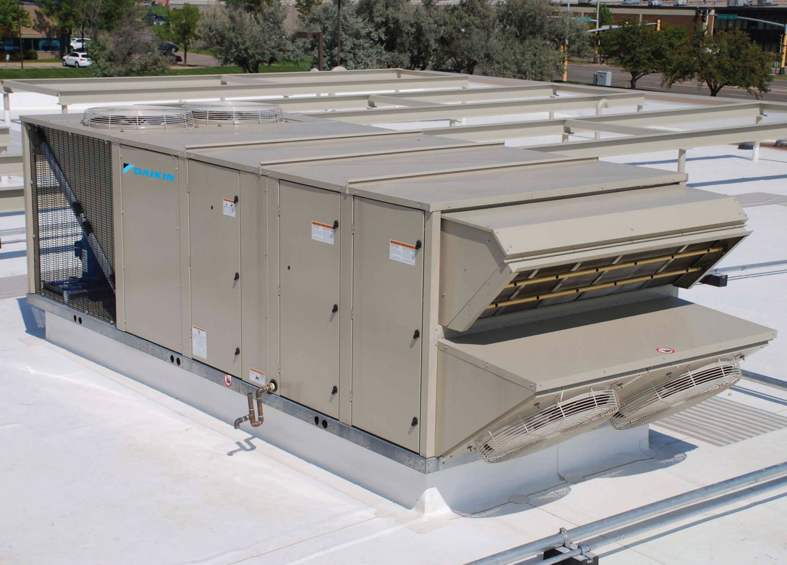 Commercial HVAC air conditioning unit on building rooftop with trees and streets in background.