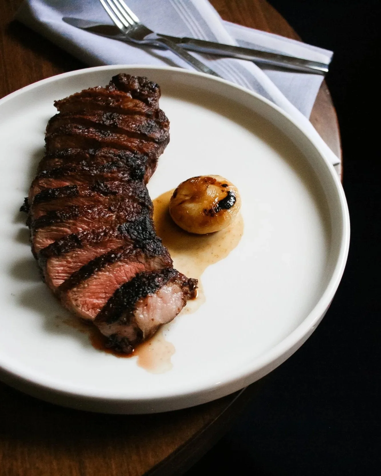 Grilled medium-rare steak slices with a grilled onion on a white plate.