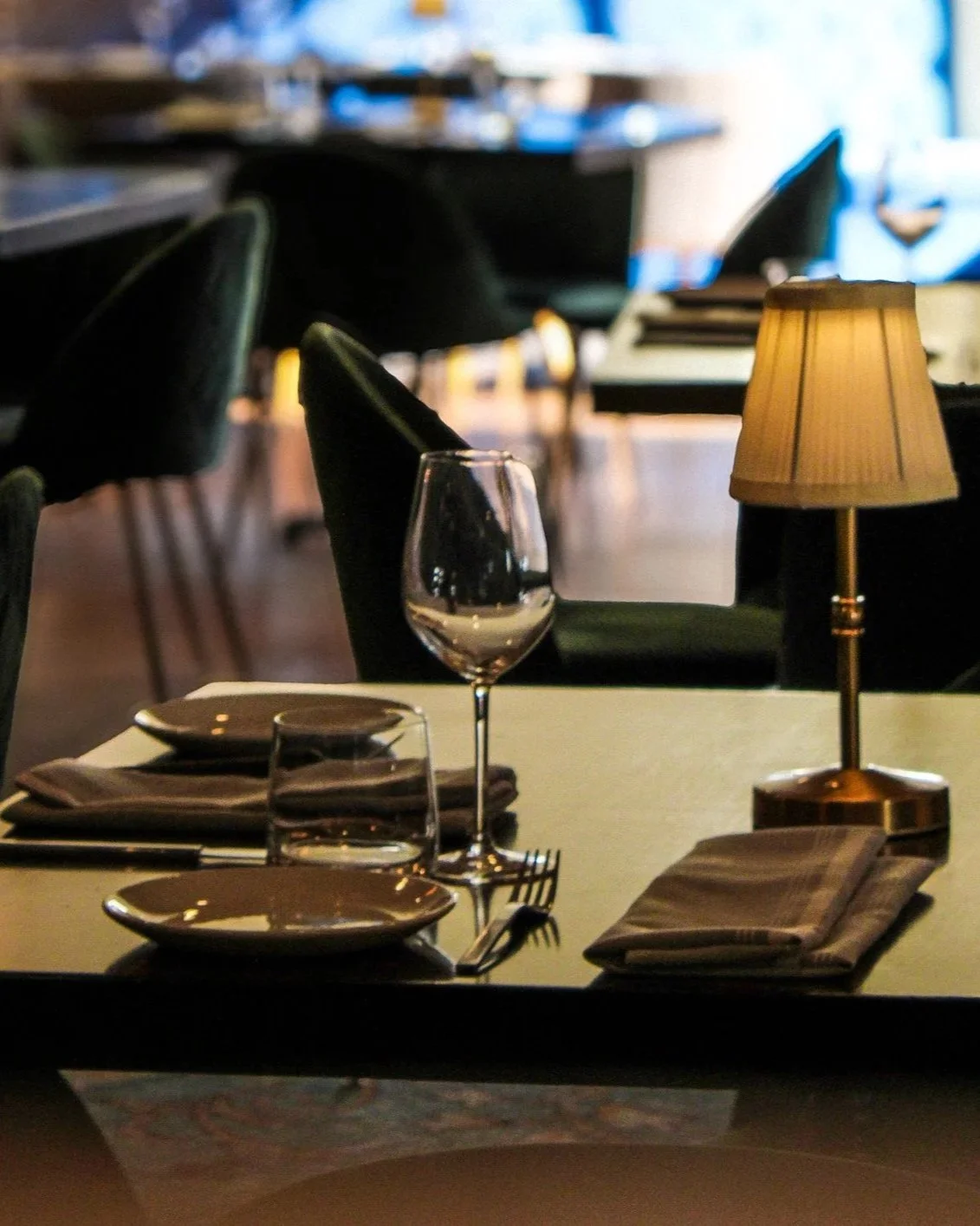 Elegant restaurant table set with a wine glass, water glass, napkin, plate, and a small table lamp.