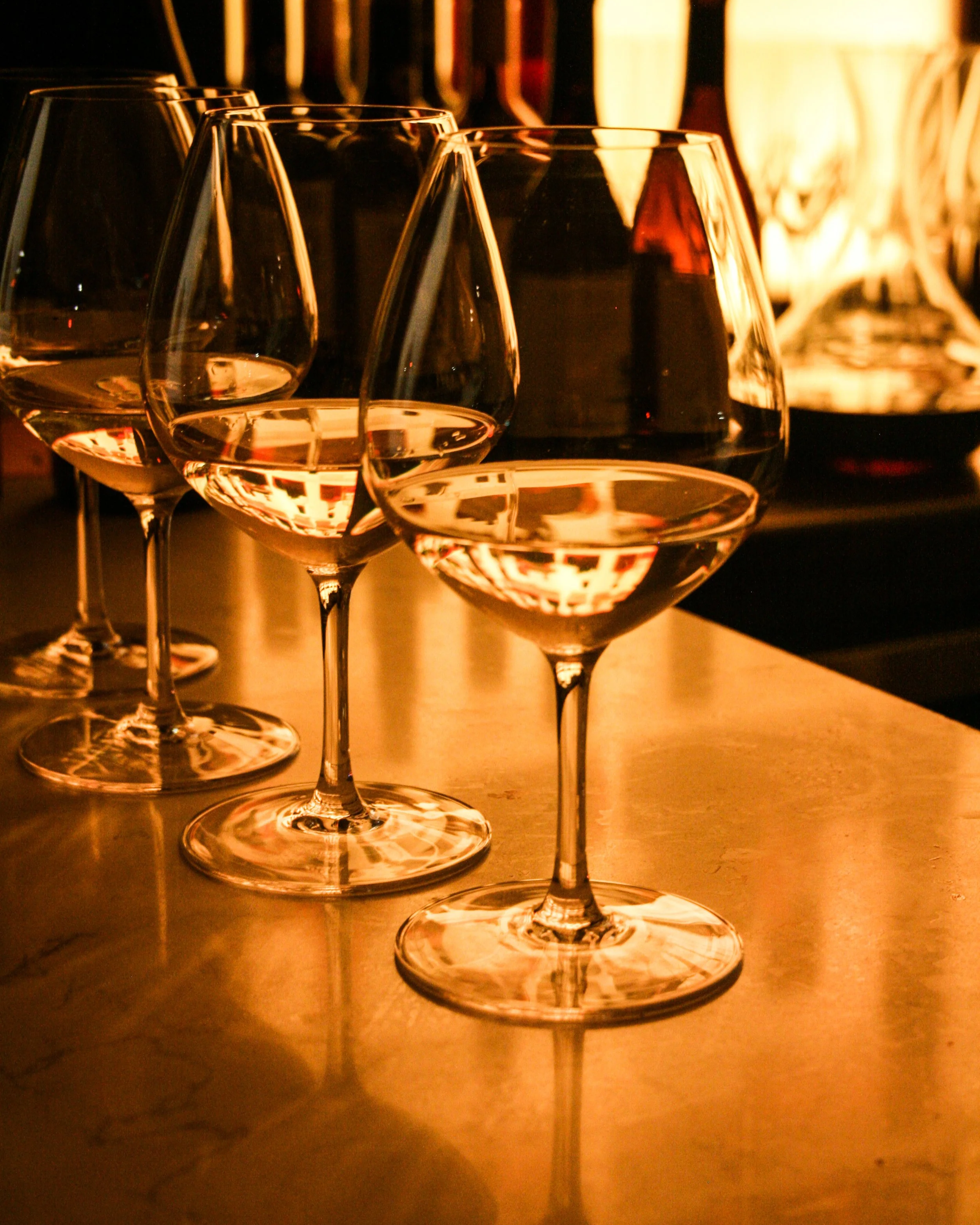 Four wine glasses filled with white wine on a wooden surface, reflecting warm amber lighting.