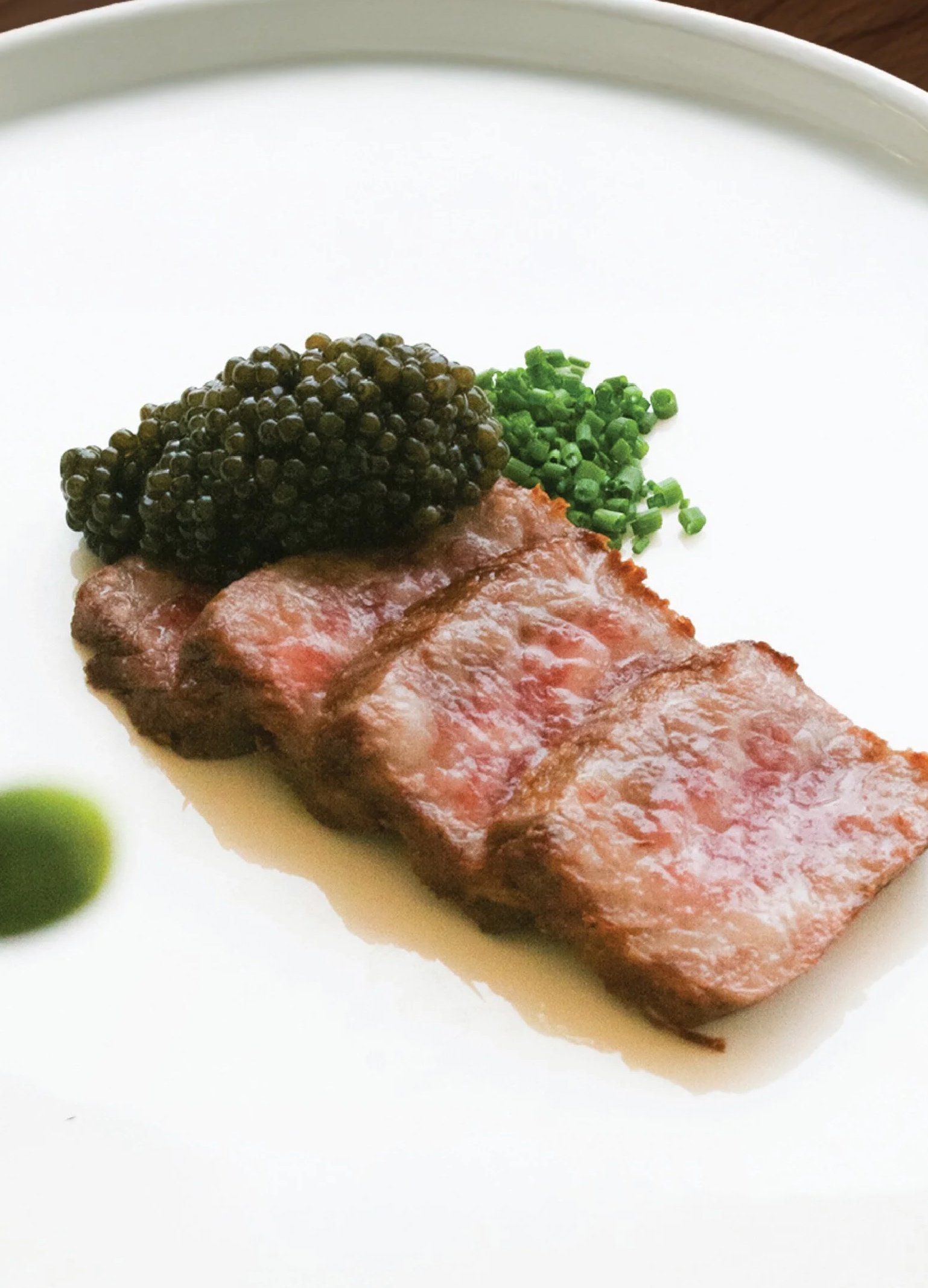 Thinly sliced Japanese wagyu beef, topped with caviar, and chopped chives on a simple white plate.