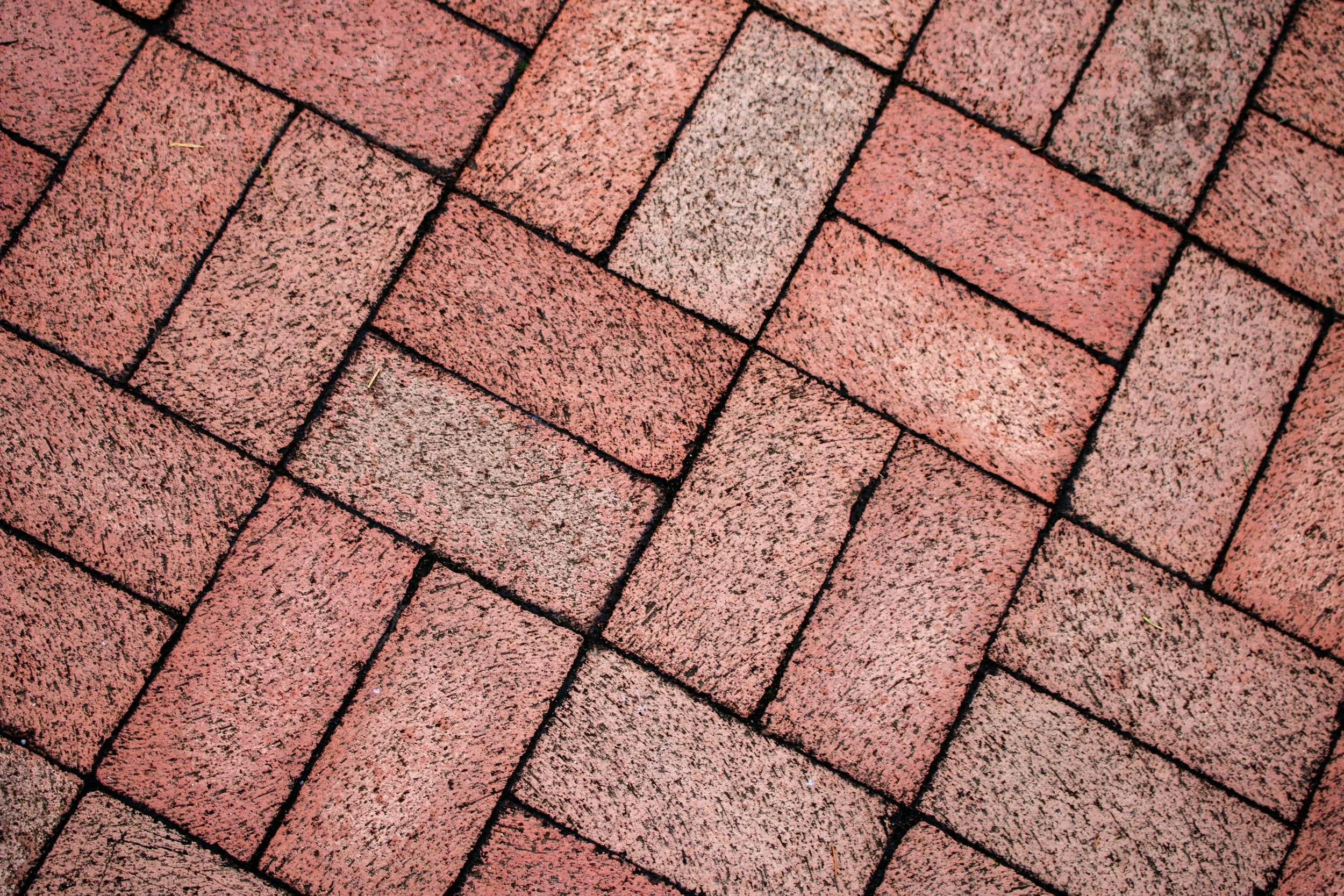Close-up of red brick pavement with uniform rectangular bricks arranged in a herringbone pattern.
