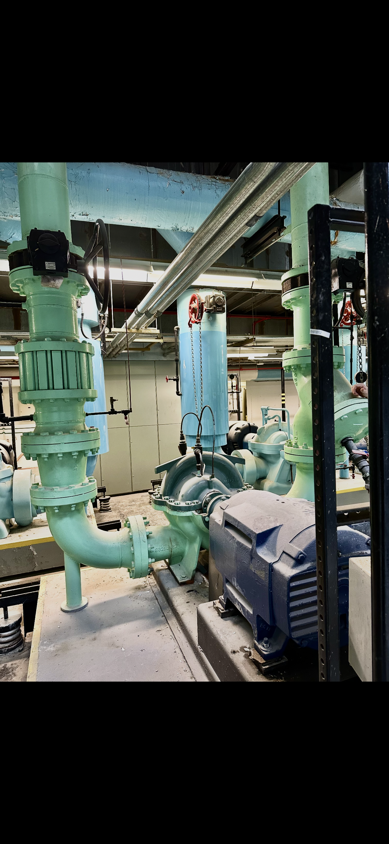 Industrial mechanical room with green and blue pipes, a motor, and valves.