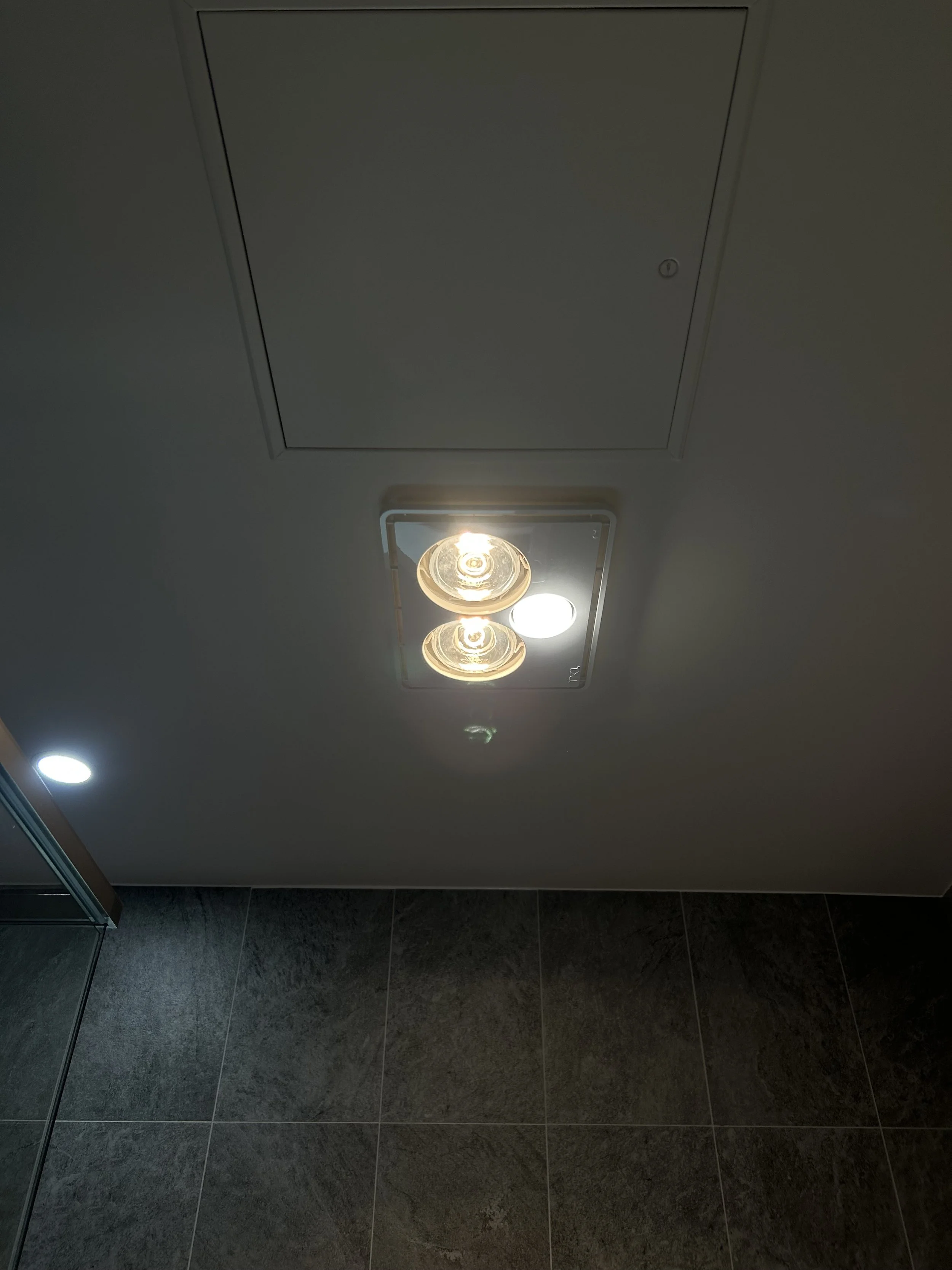 Ceiling with two overhead lights and one vent cover, with tiled walls in the background.