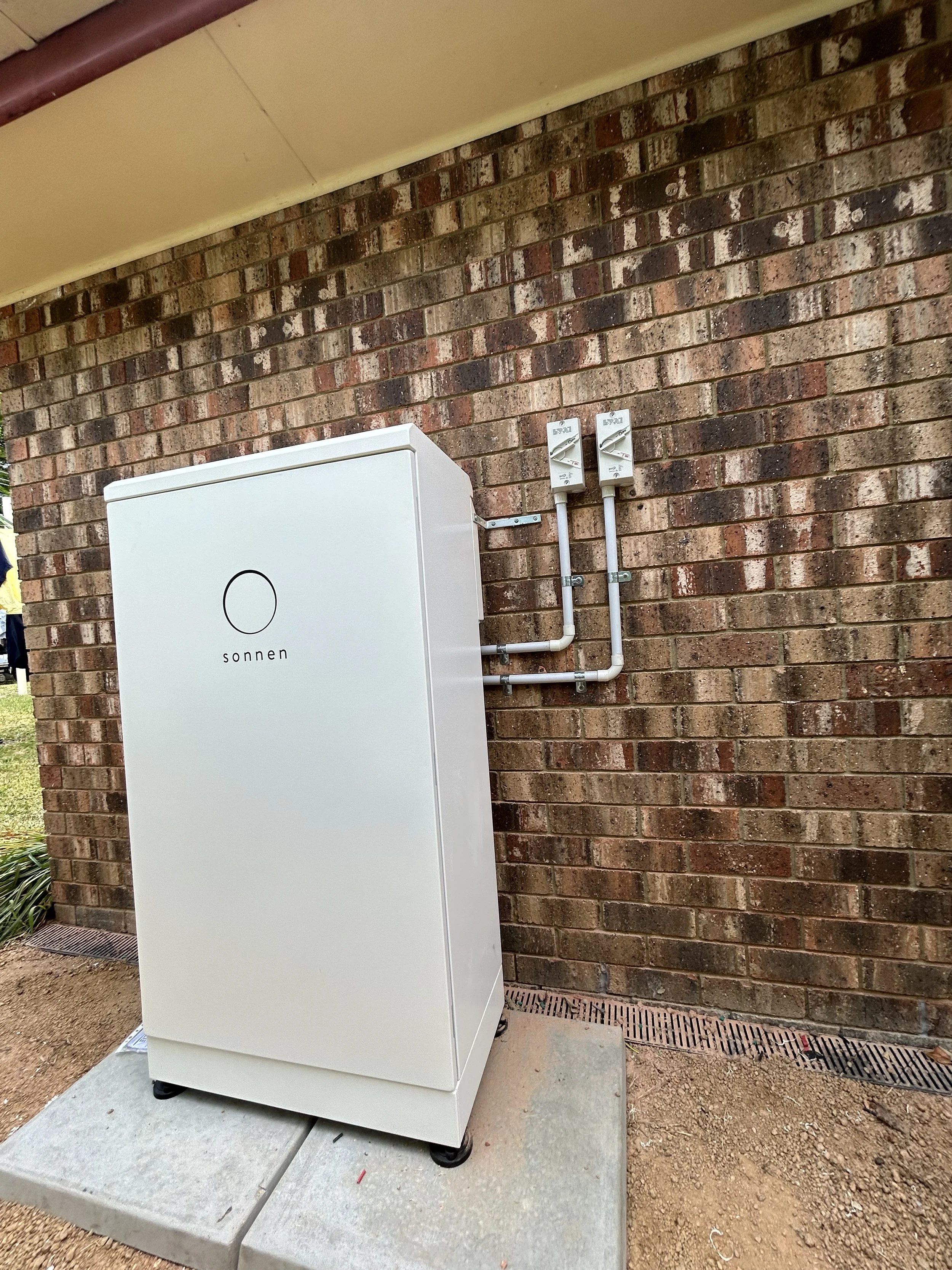 Solar power inverter unit labeled 'sonnen' installed outside on a concrete pad next to a brick wall.