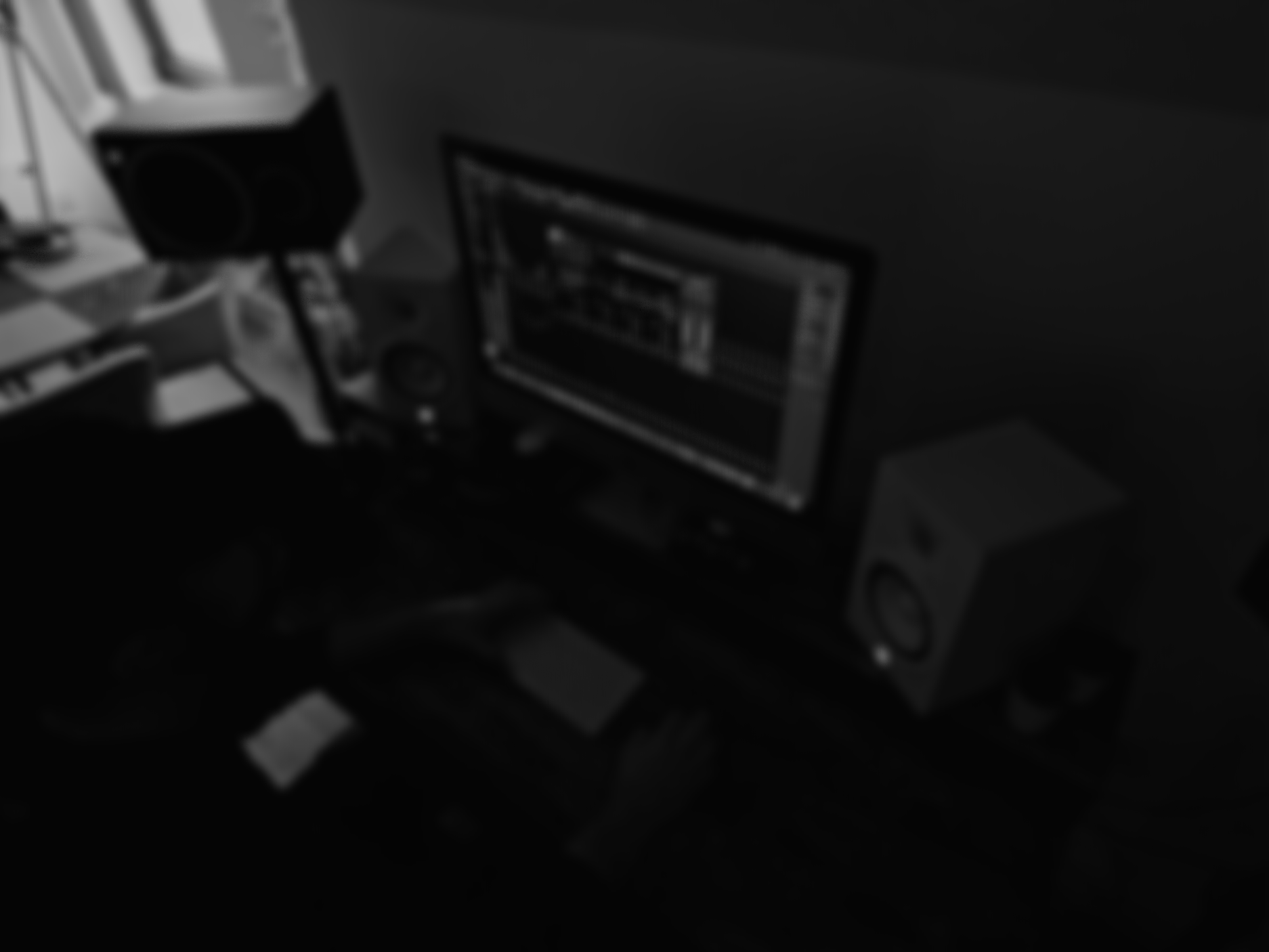 A darkened image of a music production workspace with a computer monitor displaying digital audio workstation software, surrounded by studio speakers and audio equipment.