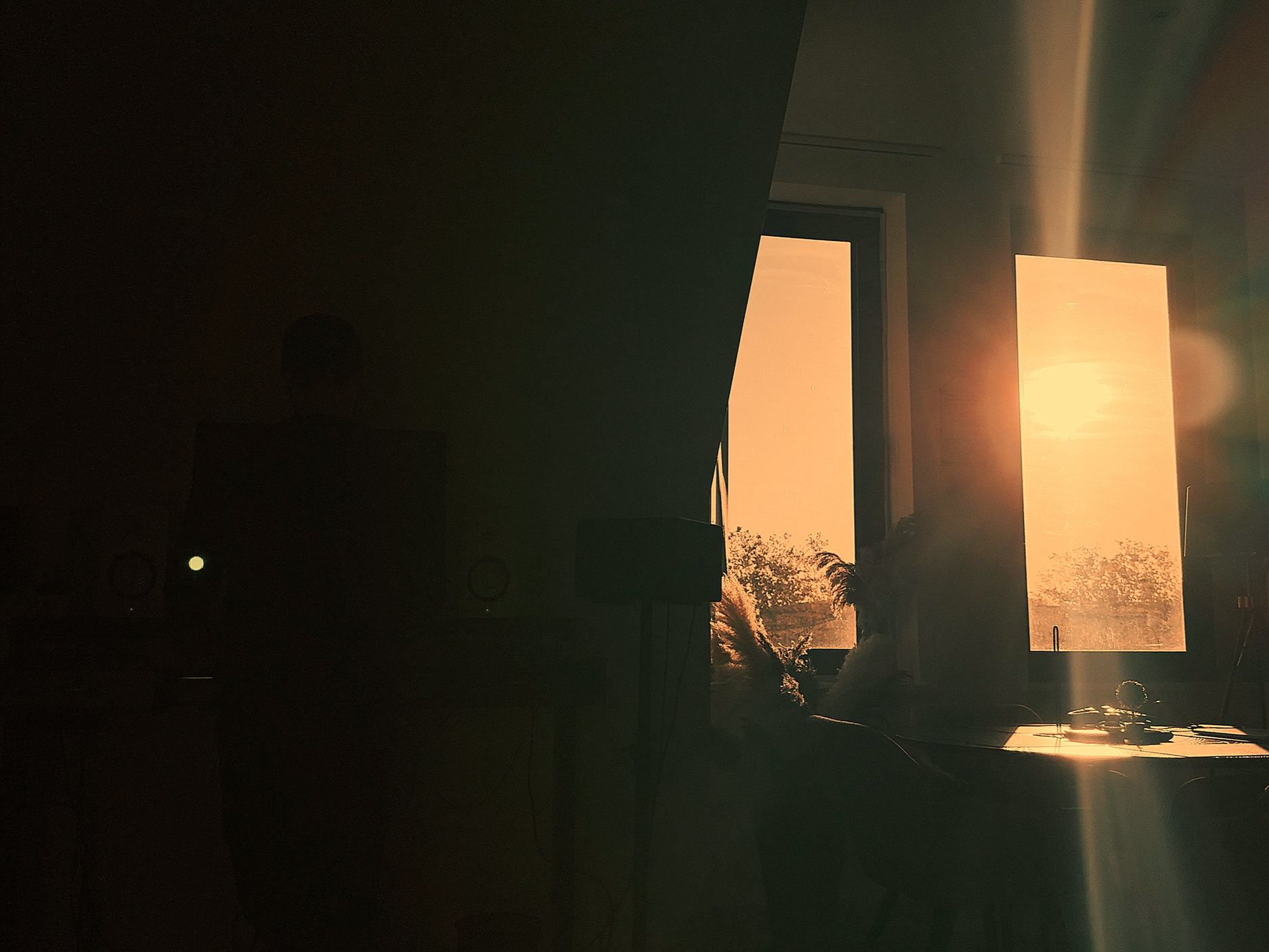 Sunrise through two open windows illuminating a room with a person working at a desk.
