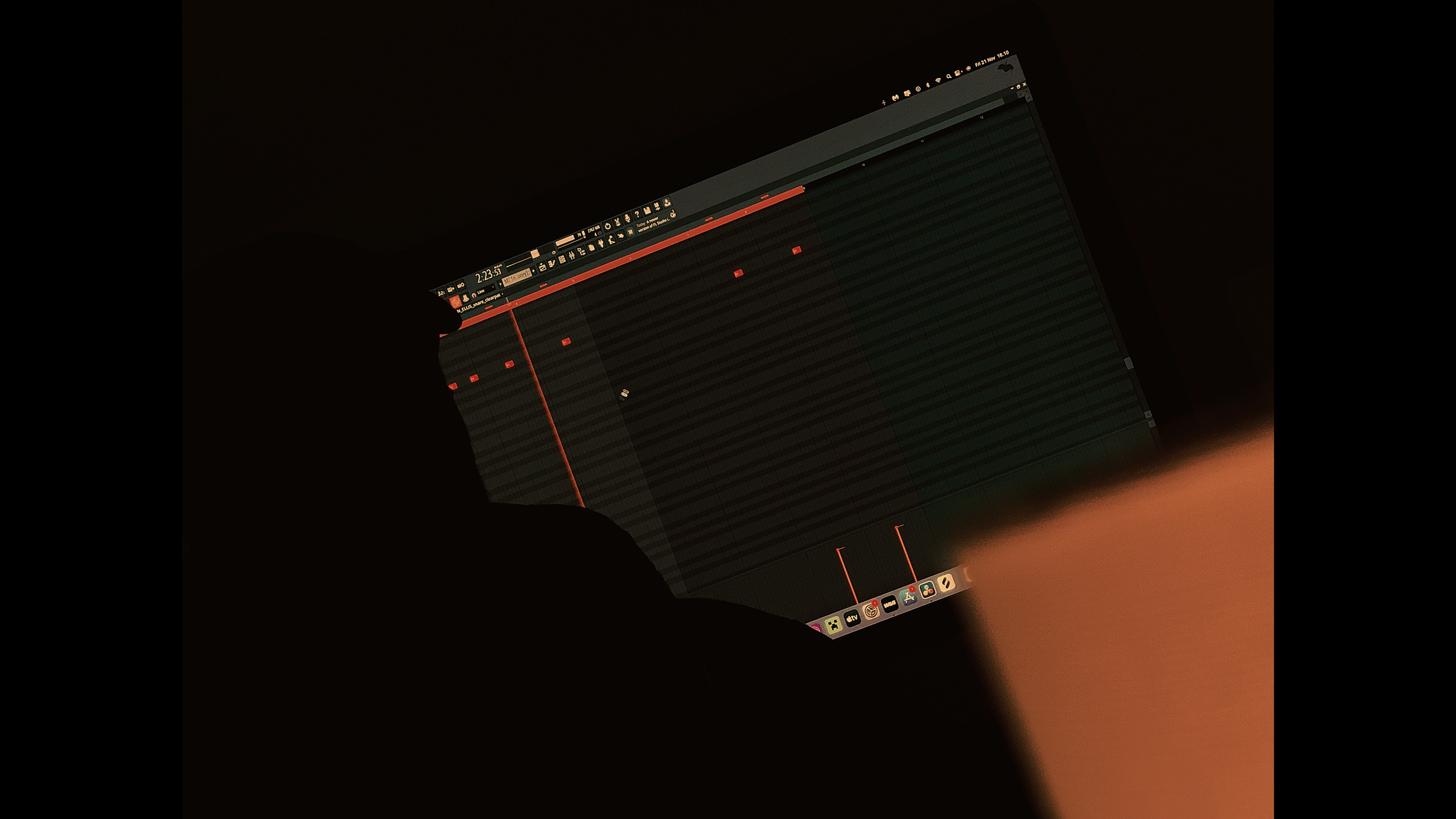 A digital audio workstation on a computer screen showing a music production interface with red track lines and waveforms, in a dark environment.